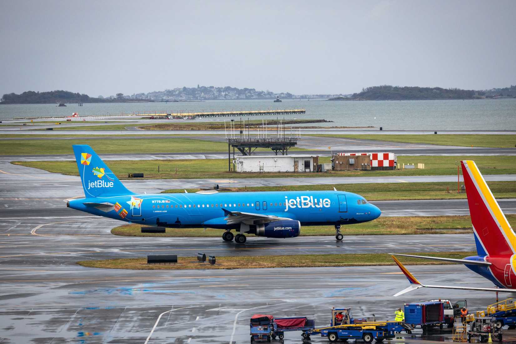 A colorful JetBlue plane taxiing in Boston with water in the background