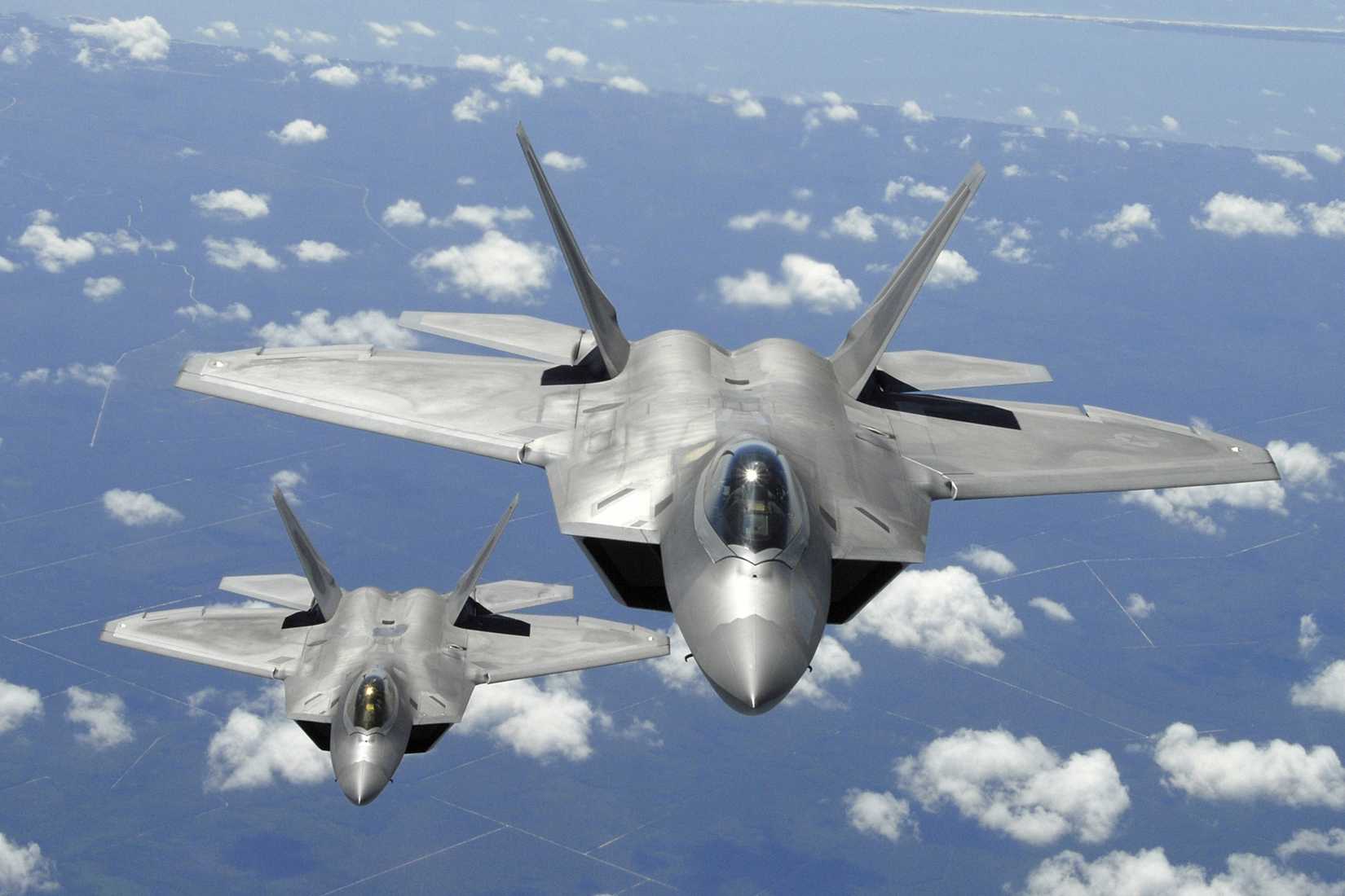 Air Force F-22 Raptor aircraft fly in trail behind a KC-135R Stratotanker.
