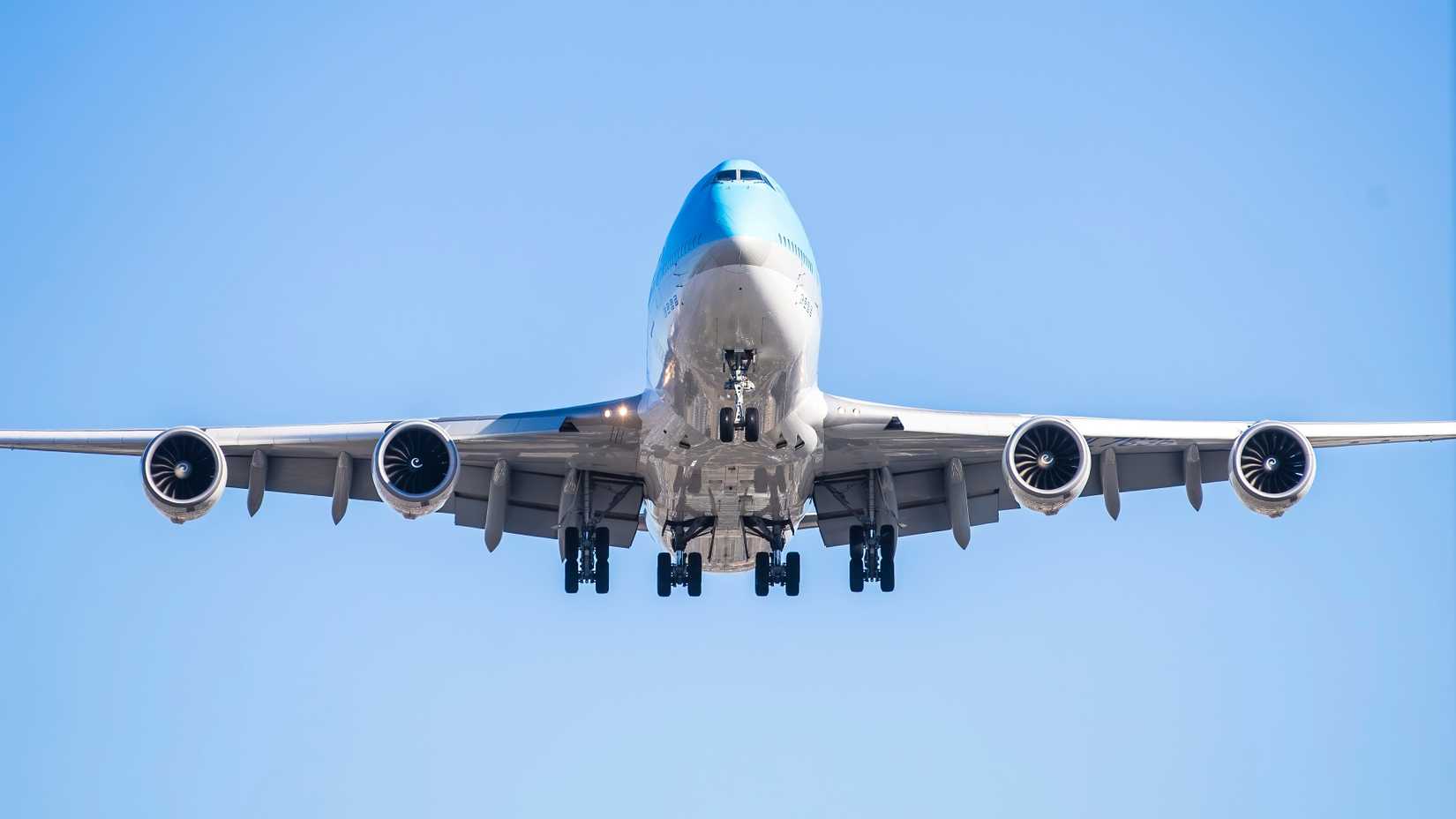 Boeing 747-8 aircraft in flight, viewed head-on, with landing gear extended against a clear blue sky.