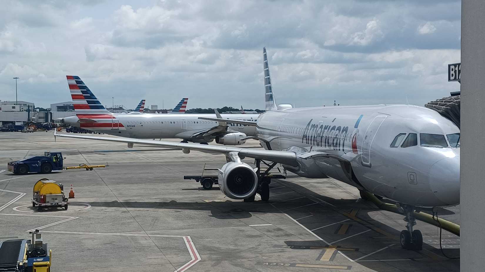 Several American Airlines planes stand at the terminal gates under a cloudy sky at Charlotte Douglas International Airport.