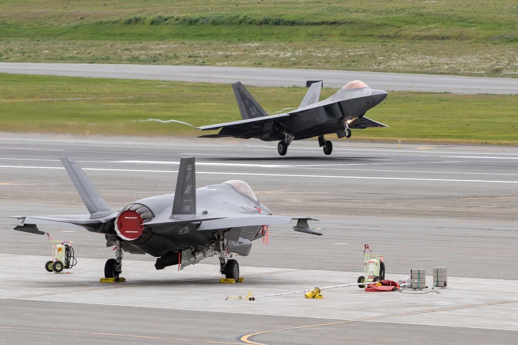 Air Force F-22 Raptor, assigned to the 3rd Wing, lands in front of a 354th Fighter Wing F-35 Lightning II.