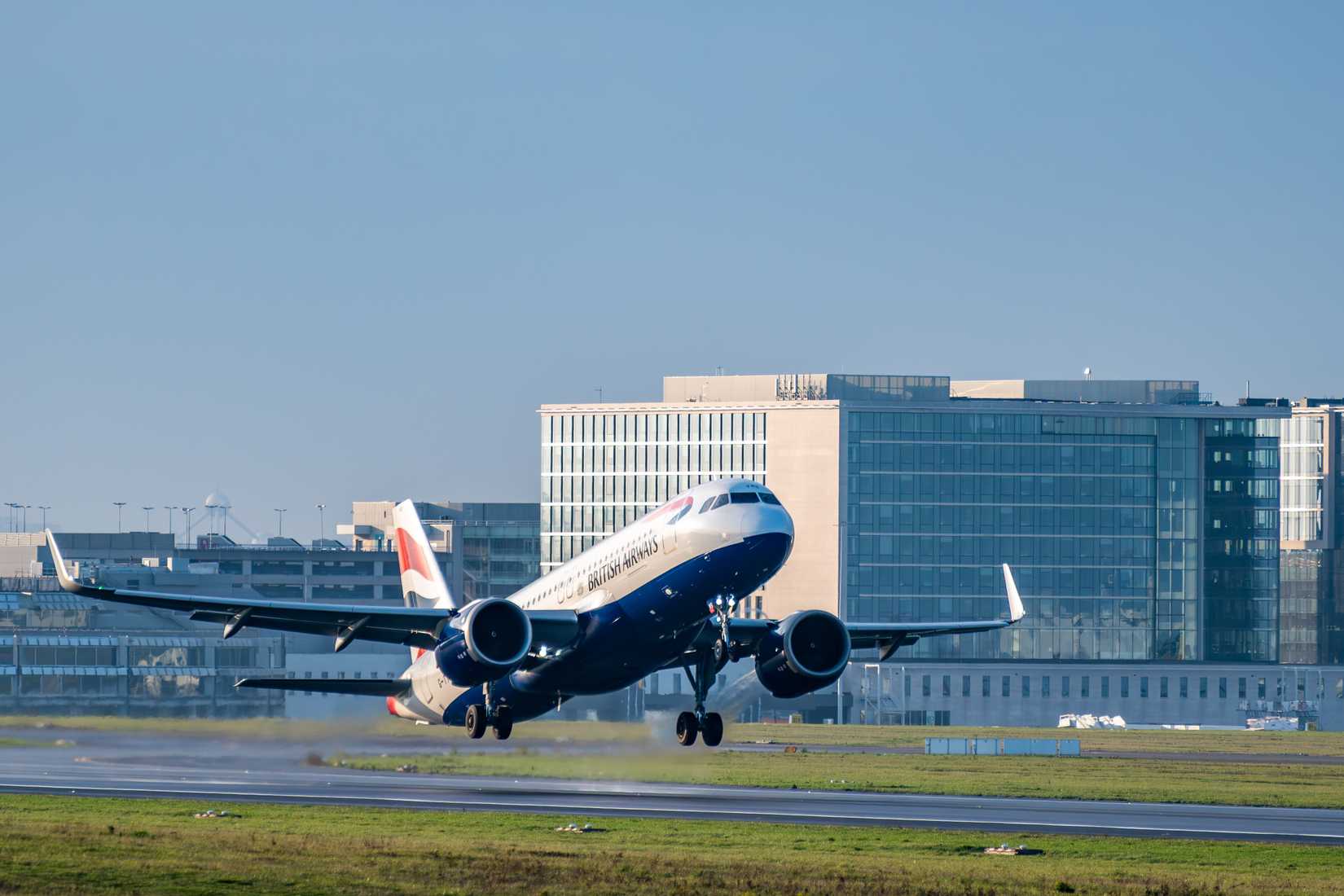 British Airways Airbus A320 passenger jet taking off from Brussels Airport with modern airport buildings in background.