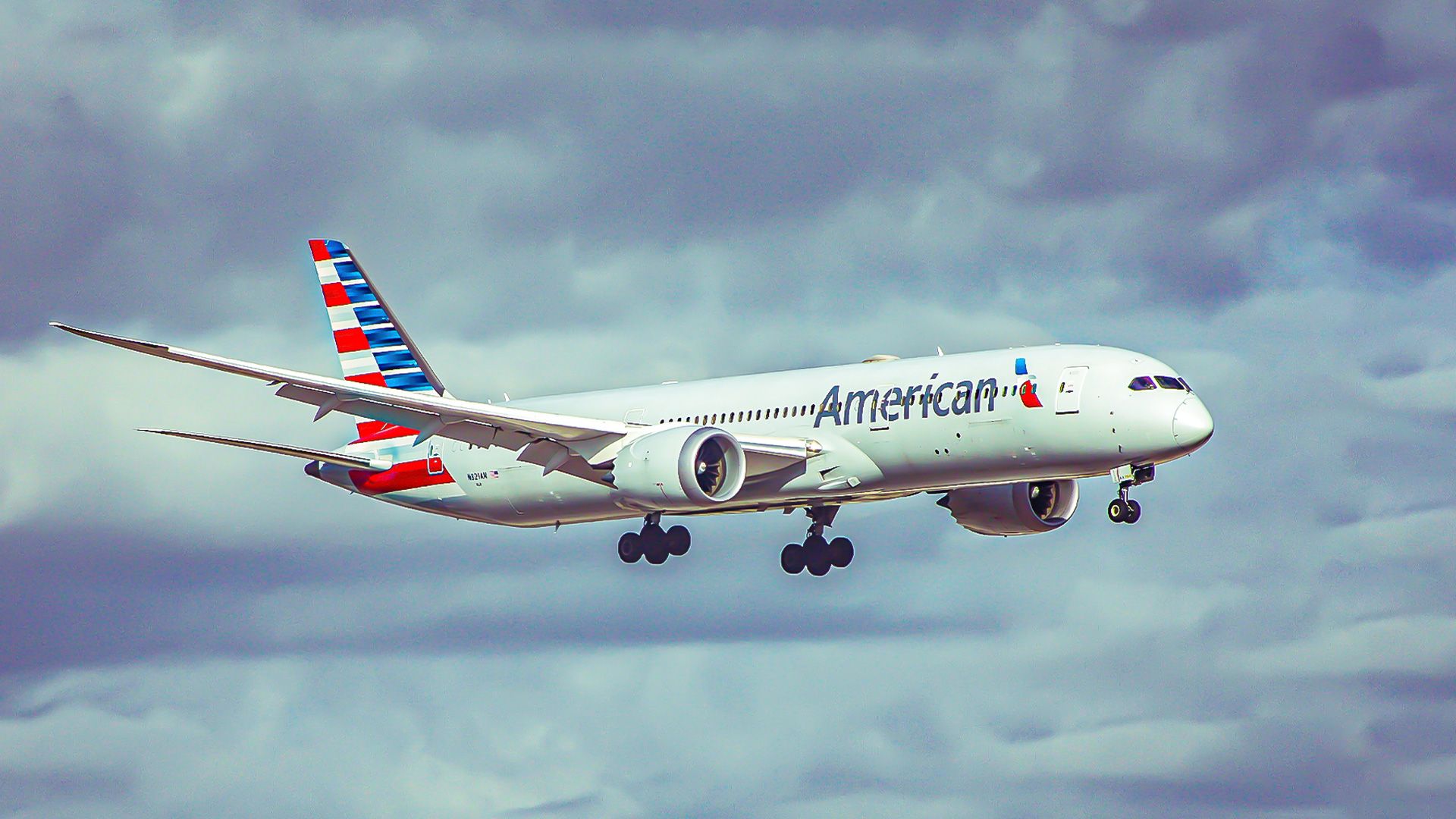 An American AIrlines Boeing 787 flying across cloudy skies
