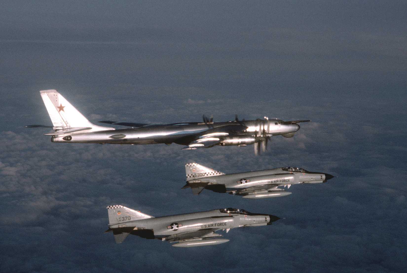 Air-to-air right side view of a Soviet Tu-95 Bear aircraft, top, being observed by two U.S. Air Force F-4 Phantom II