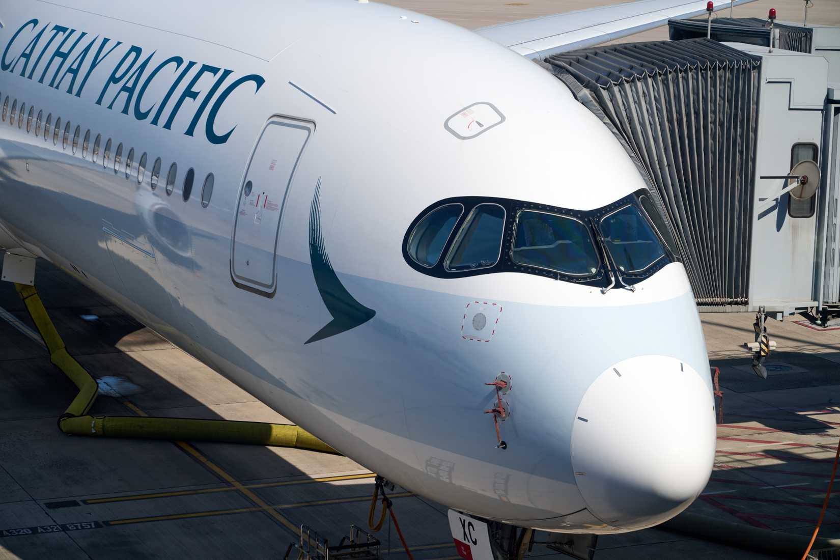 Cathay Pacific A350 at HKG gate with jet bridge, Korean Air tail visible, arched terminal and mountains under clear blue sky.