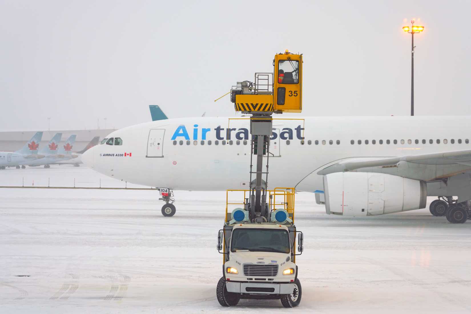 De-icing trucks removing frost and ice near airplanes during a winter snow storm at the Toronto Pearson International Airport (YYZ) in Canada.