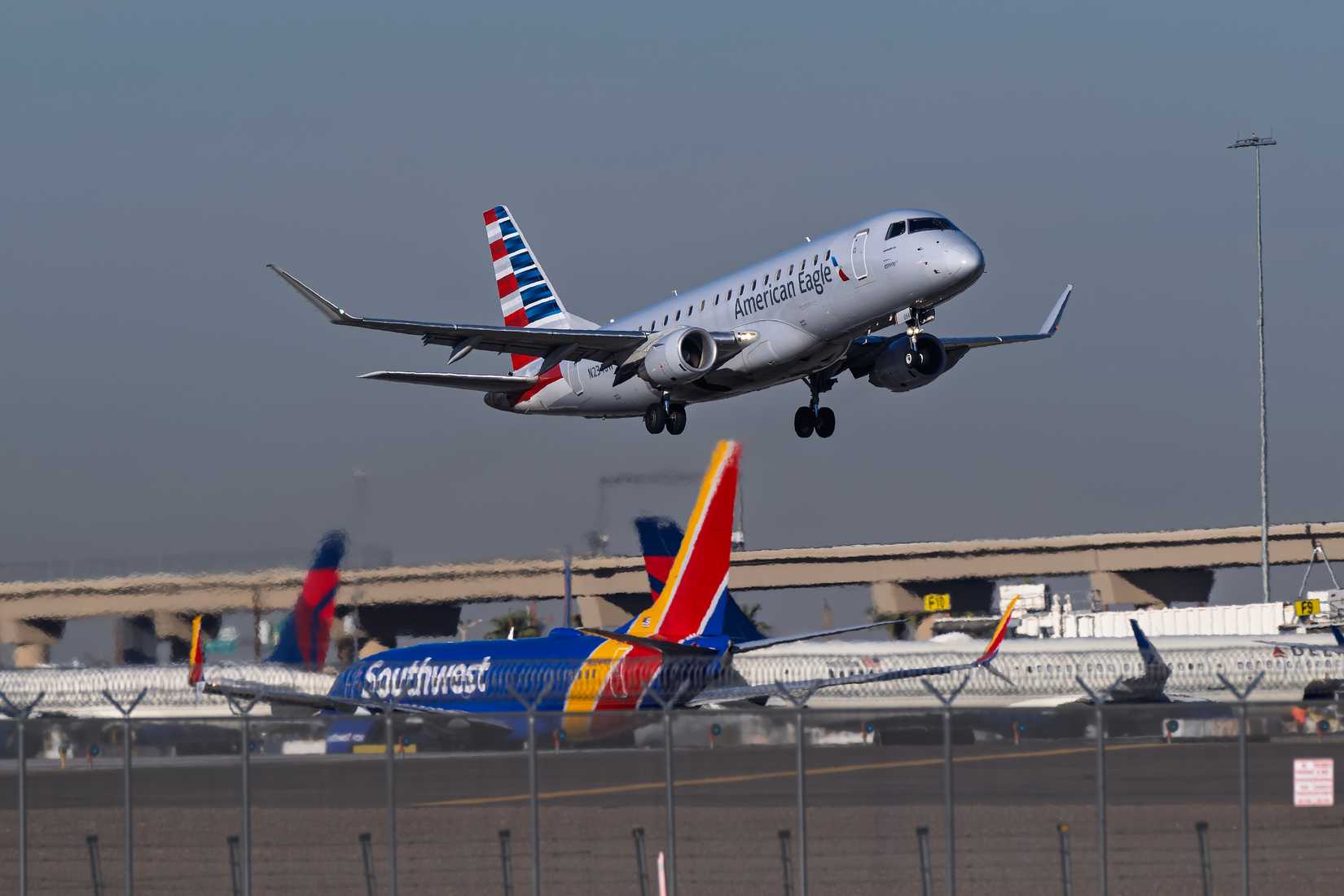 American Airlines Embraer E-175 departing; Southwest and Delta Air Lines aircraft in the background