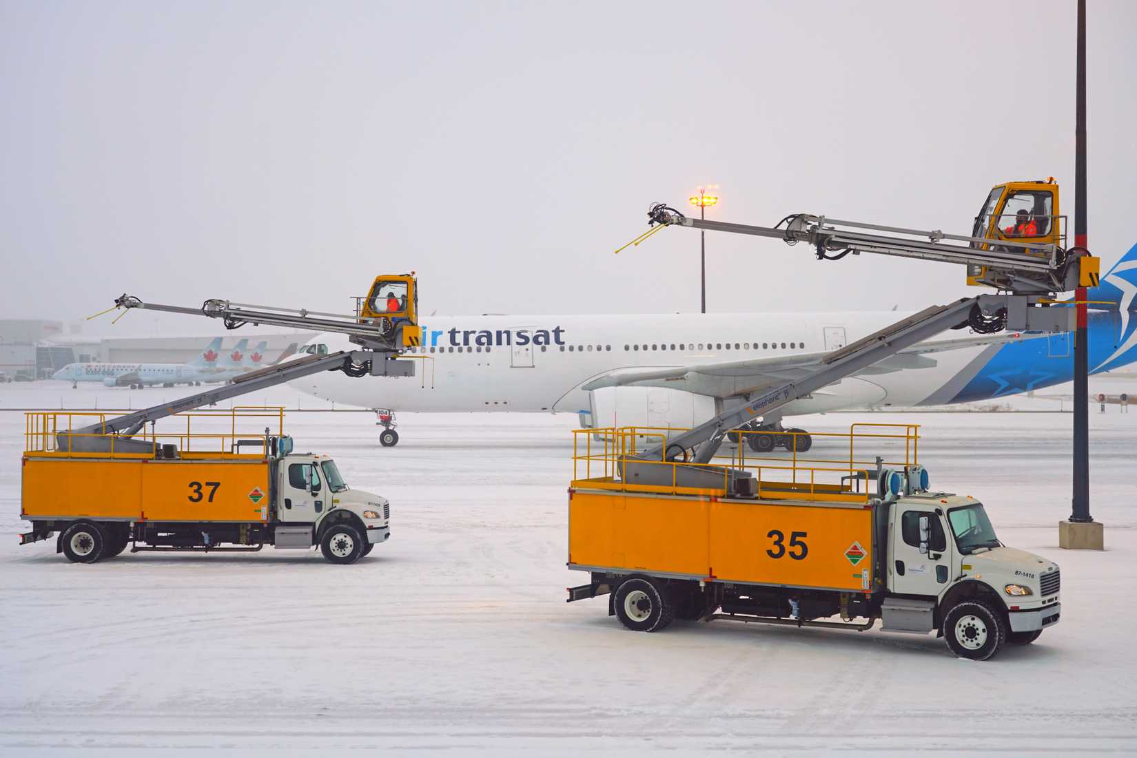 Trucks removing frost and ice near airplanes during a winter snow storm at the Toronto Pearson International Airport (YYZ)