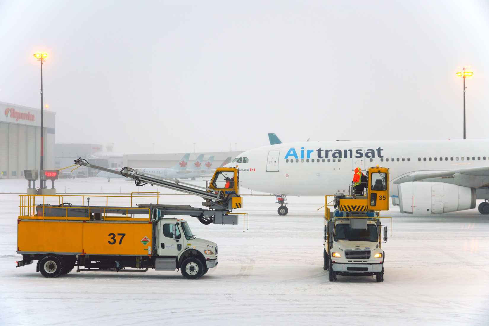 Trucks removing snow and ice near airplanes during a winter snow storm at the Toronto Pearson International Airport (YYZ).