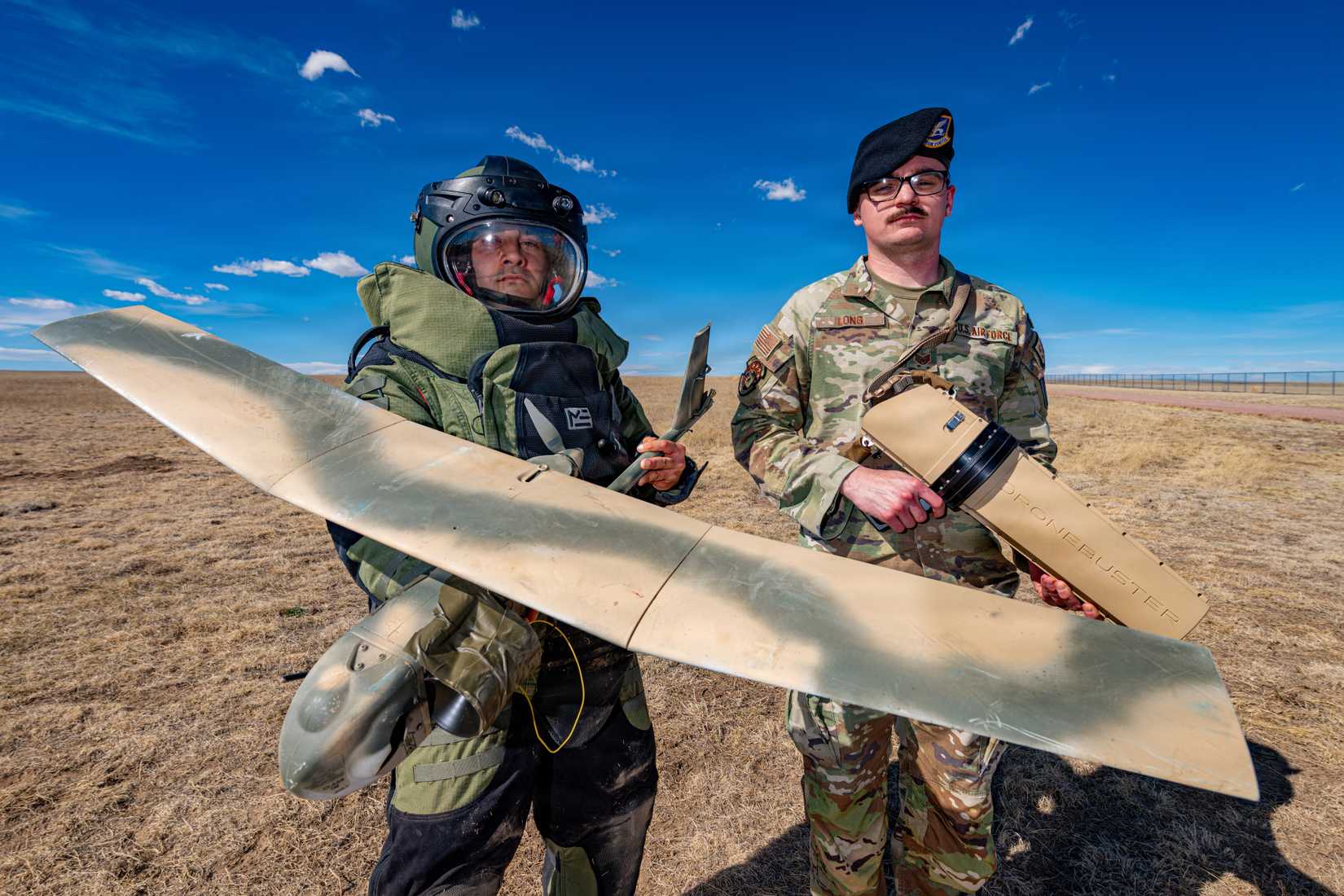 Air Force explosive ordnance disposal technician and noncommissioned officer in charge, pose for a photo with a drone buster gun and dead UAV at Schriever Space Base.