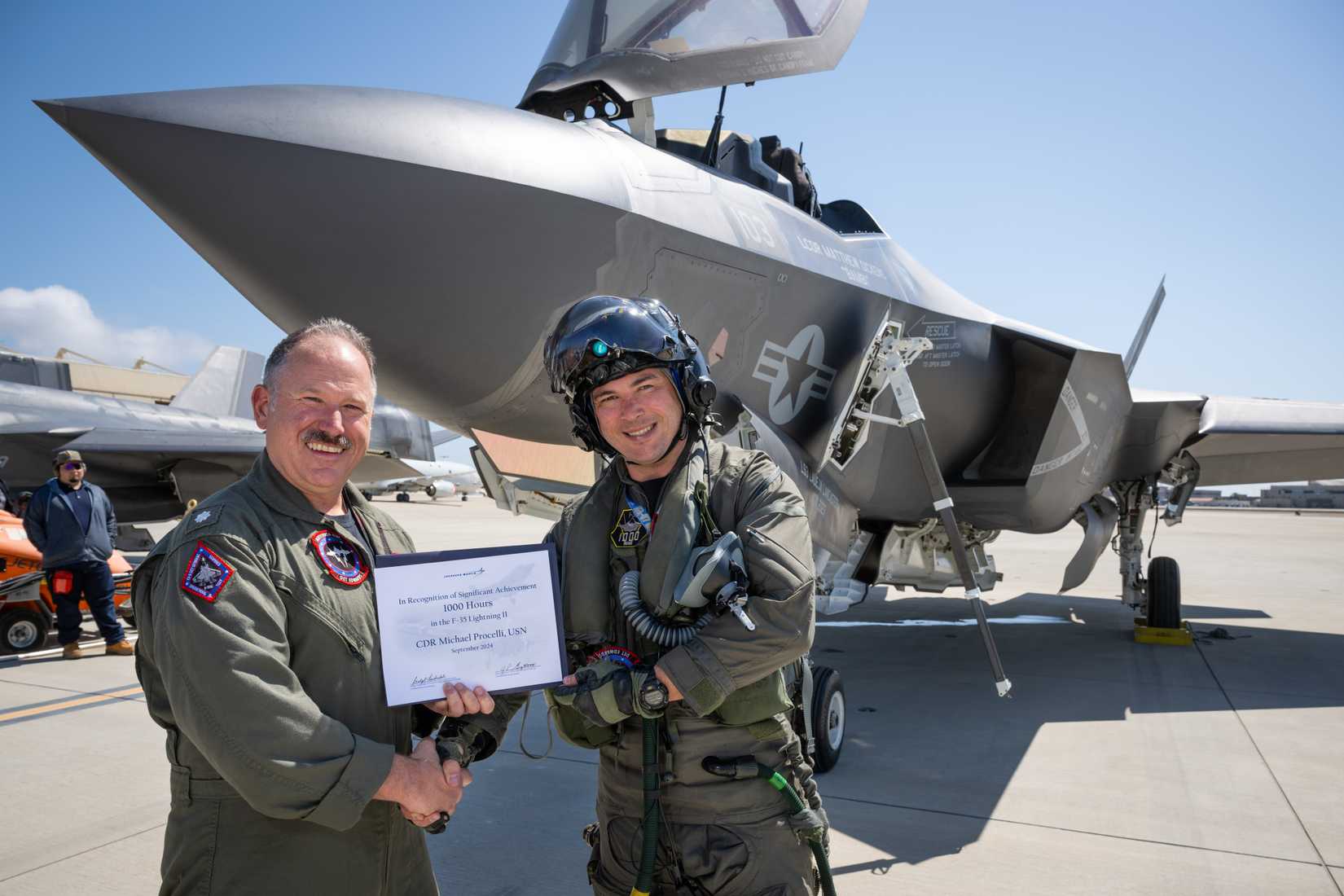 Air Test and Evaluation Squadron (VX) Nine, Cmdr. Michael “HFM” Huntsman, left, presents a certificate to Cmdr. Michael “Squintz” Procelli for reaching the 1,000-hour milestone flying the F-35C
