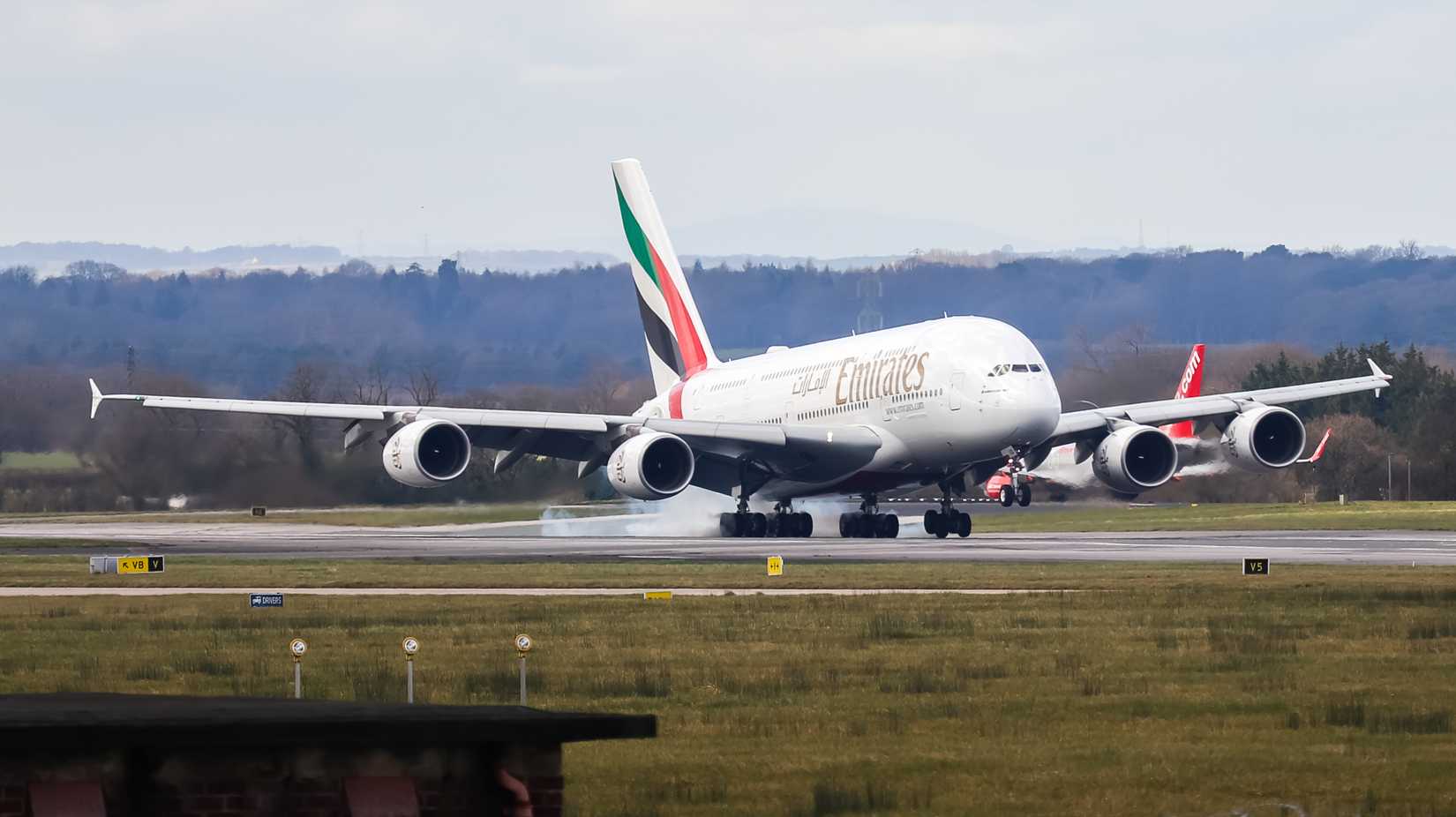 Emirates A380 landing at an airport, surrounded by greenery