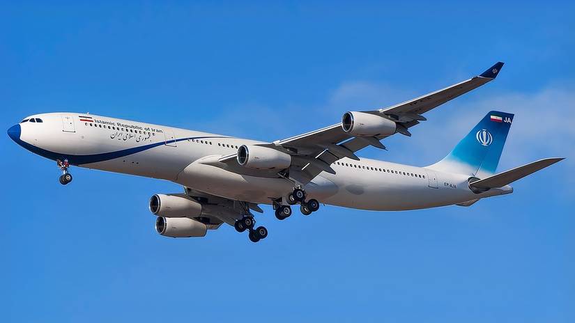 An Airbus A340-300 operated by the Islamic Republic of Iran, registration EP-AJA, is shown in flight against a clear blue sky. The aircraft features a white fuselage with "Islamic Republic of Iran" written in both English and Persian, a blue nose cone, and a blue gradient tail bearing a white national emblem and the Iranian flag. Its landing gear is deployed as it prepares for approach.