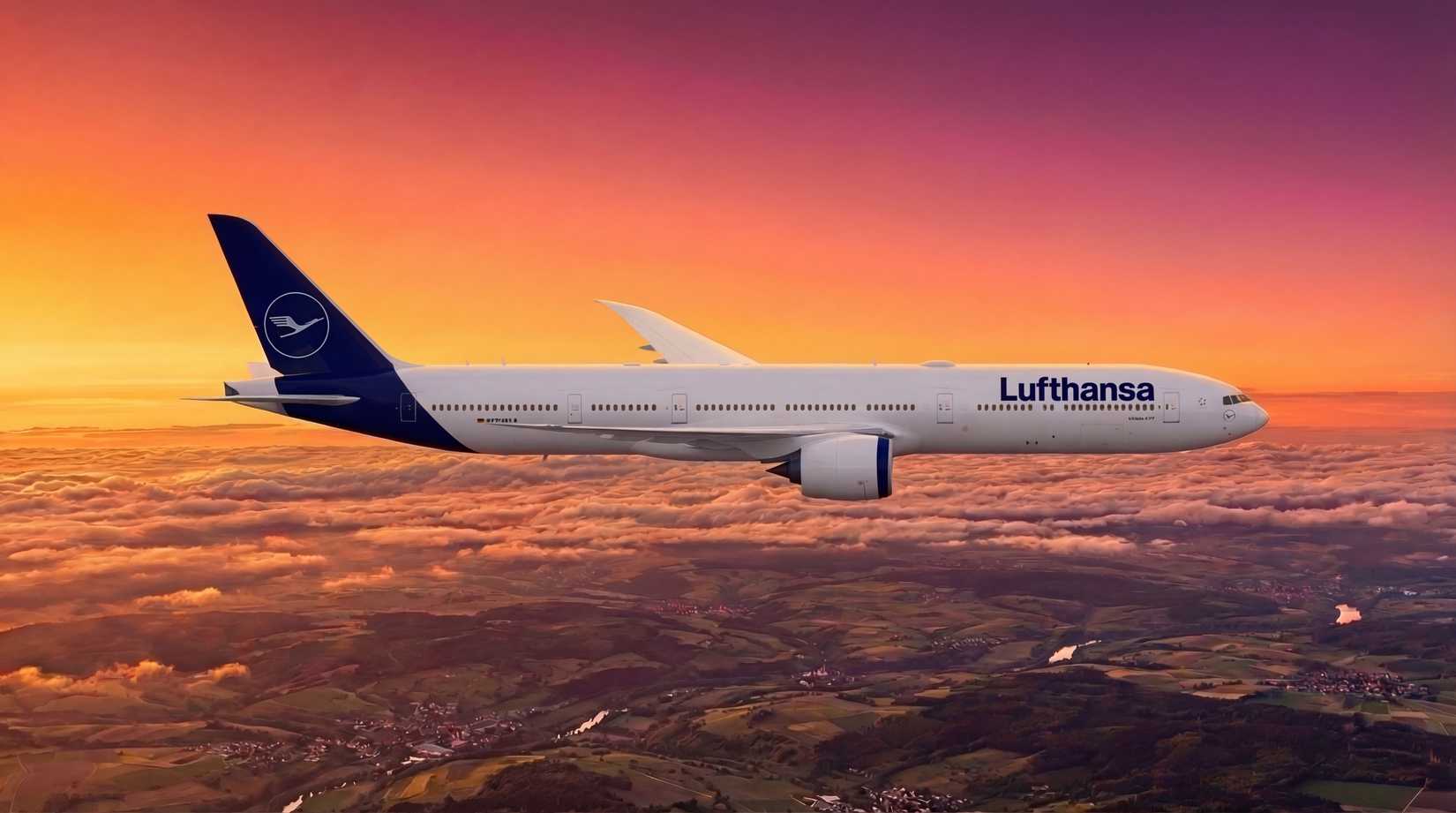 A Lufthansa wide-body aircraft cruises above a cloud layer at sunset, with a vivid orange and pink sky above and a patchwork of green fields visible below