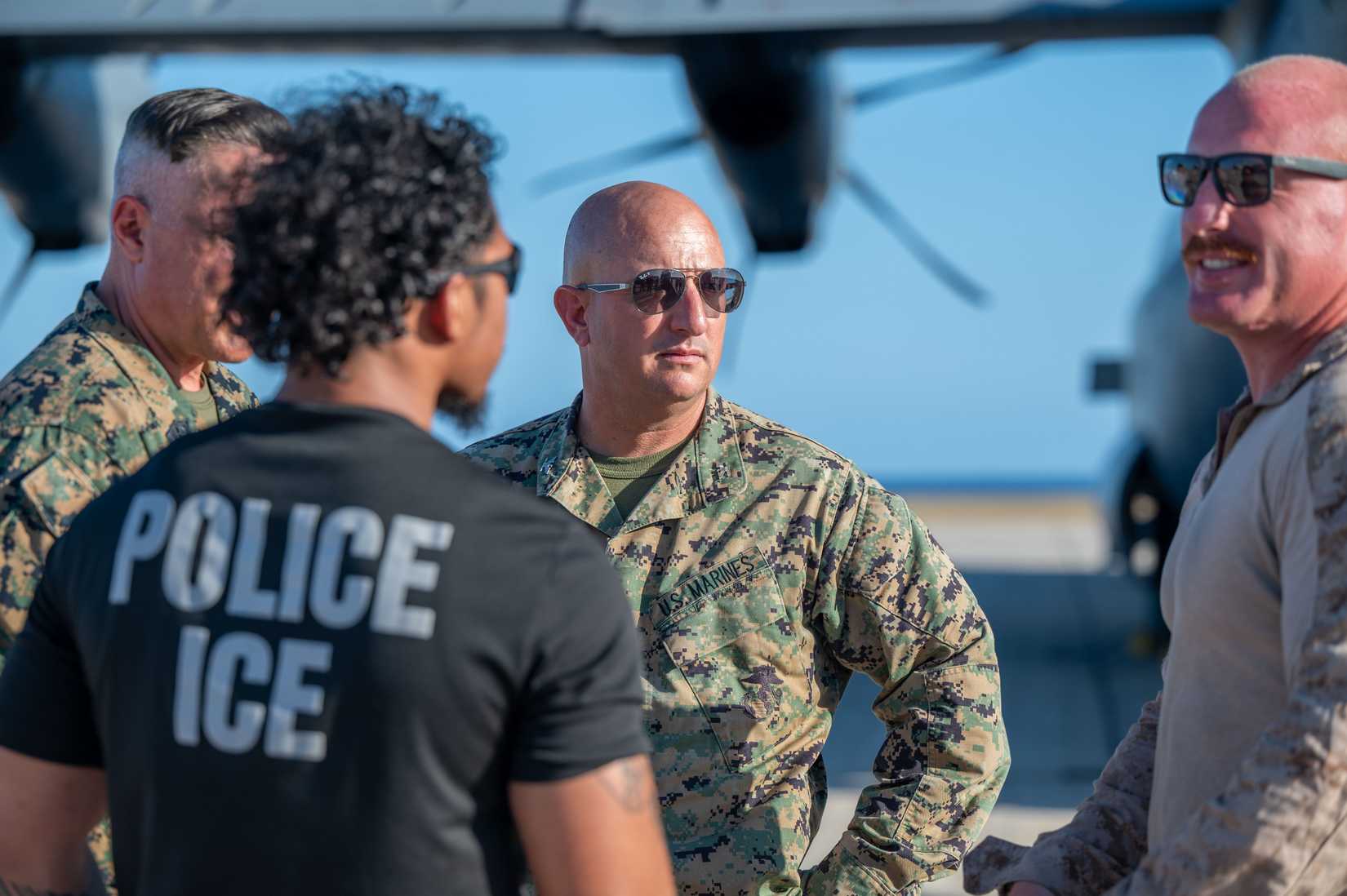 Marines assigned to Joint Task Force Southern Guard speak with an Immigration and Customs Enforcement officer during an illegal alien arrival flight at Naval Station Guantanamo Bay, Cuba, 2025.
