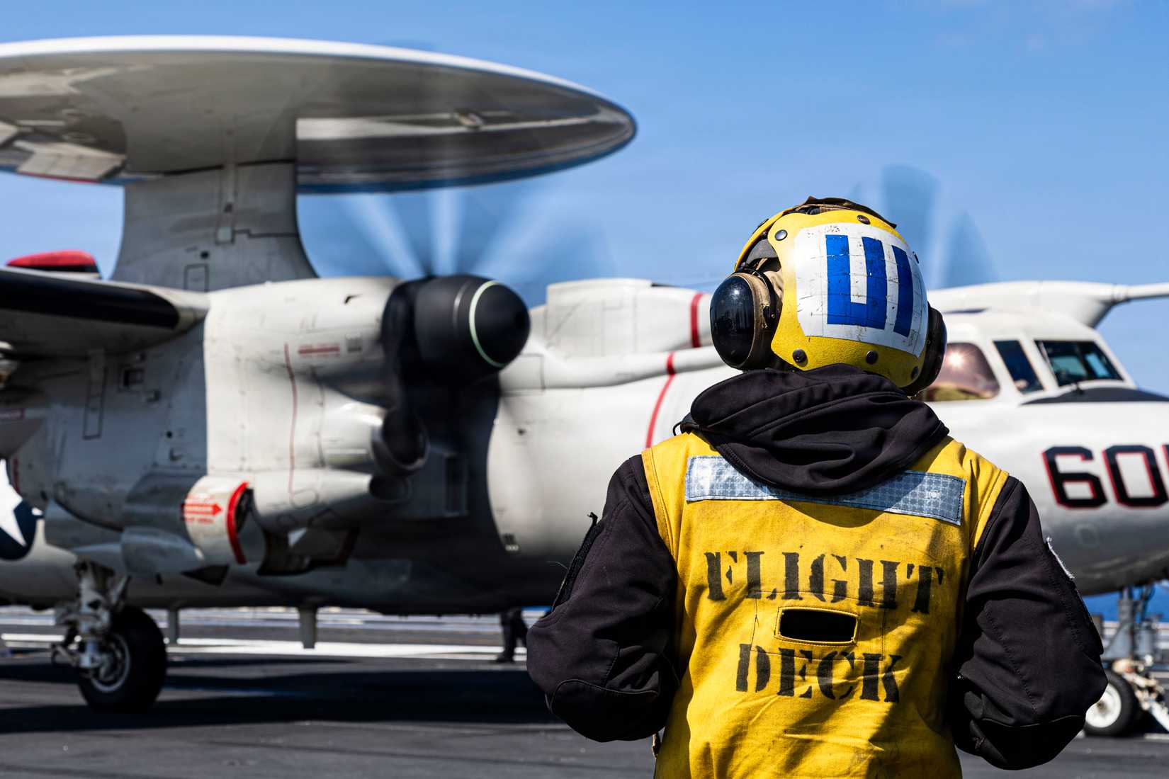 Sailor observes an E-2D Hawkeye aircraft, attached to Airborne Command and Control Squadron 124, as it taxis for launch on the flight deck.
