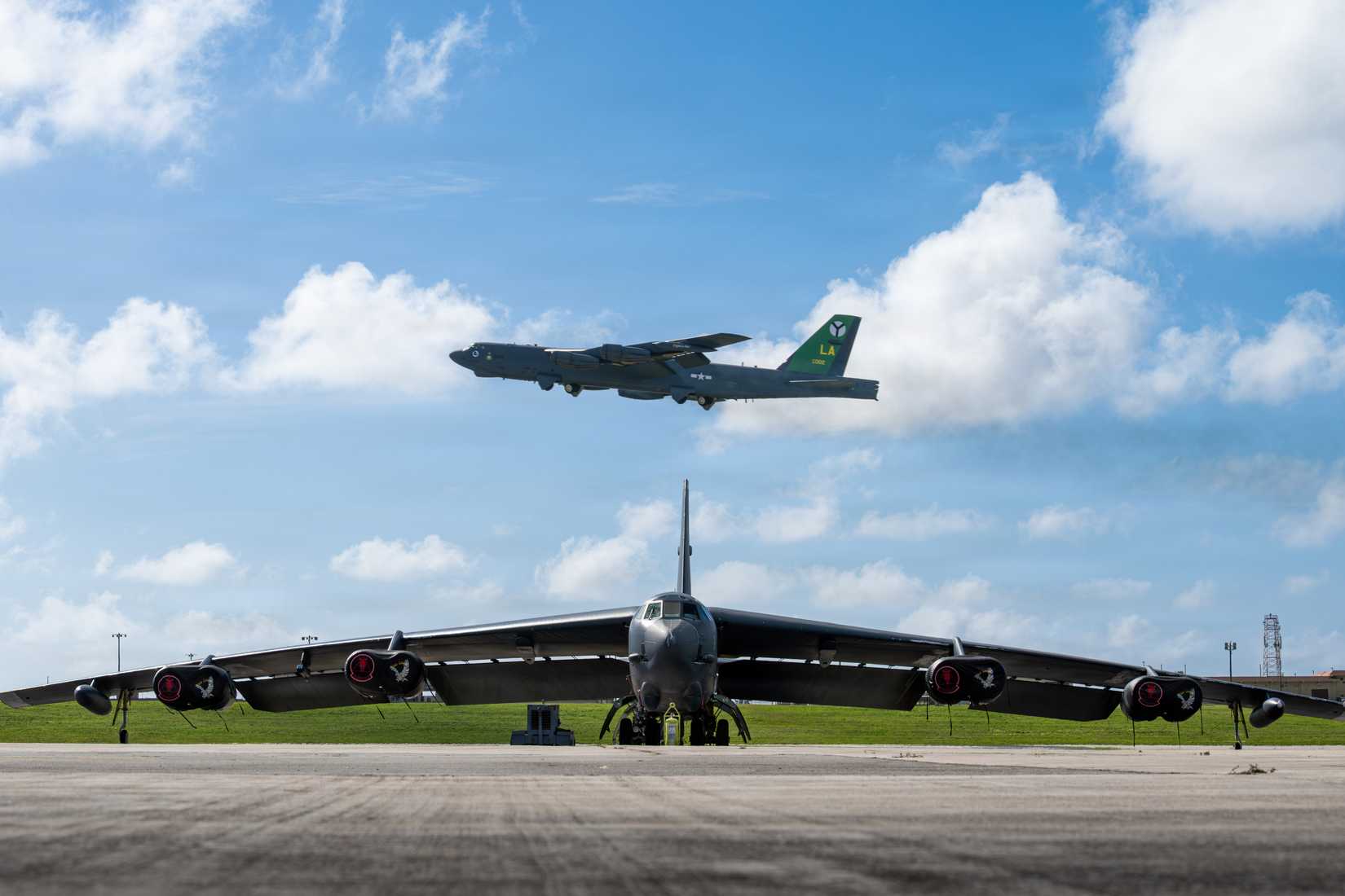 The 2nd Bomb Wing flagship B-52H Stratofortress flies over another B-52H parked on the flightline at Andersen Air Force Base, Guam, Feb. 10, 2026.