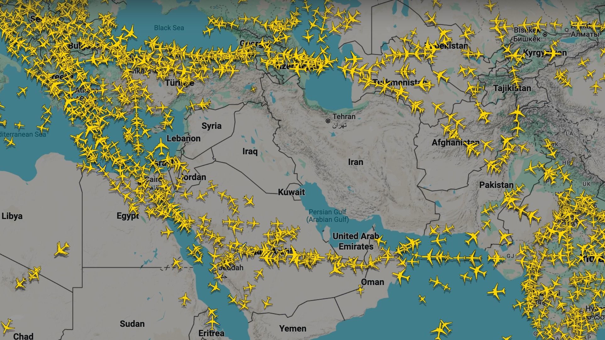 A digital flight tracking map of the Middle East, Central Asia, and surrounding regions shows a high volume of active air traffic. Hundreds of small yellow airplane icons are clustered heavily over southeastern Europe, Turkey, and the Mediterranean Sea, with a significant stream of traffic flowing through the Persian Gulf and over the United Arab Emirates. In contrast, the airspaces over several countries, including Syria, Iraq, and Afghanistan, are almost entirely devoid of aircraft icons, crea