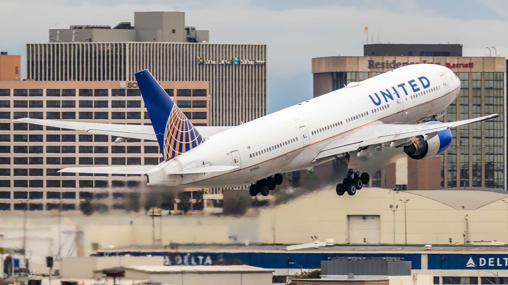 United Airlines Boein 777-200 taking off, with many buildings in the background