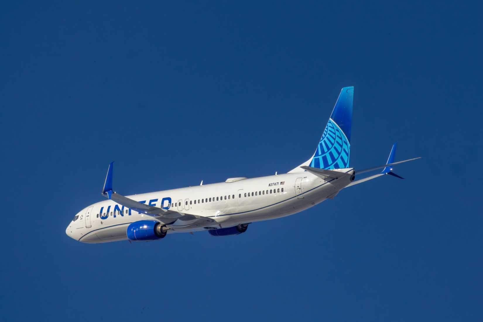 . United Airlines Boeing 737 aircraft climbing through a clear blue sky after takeoff.