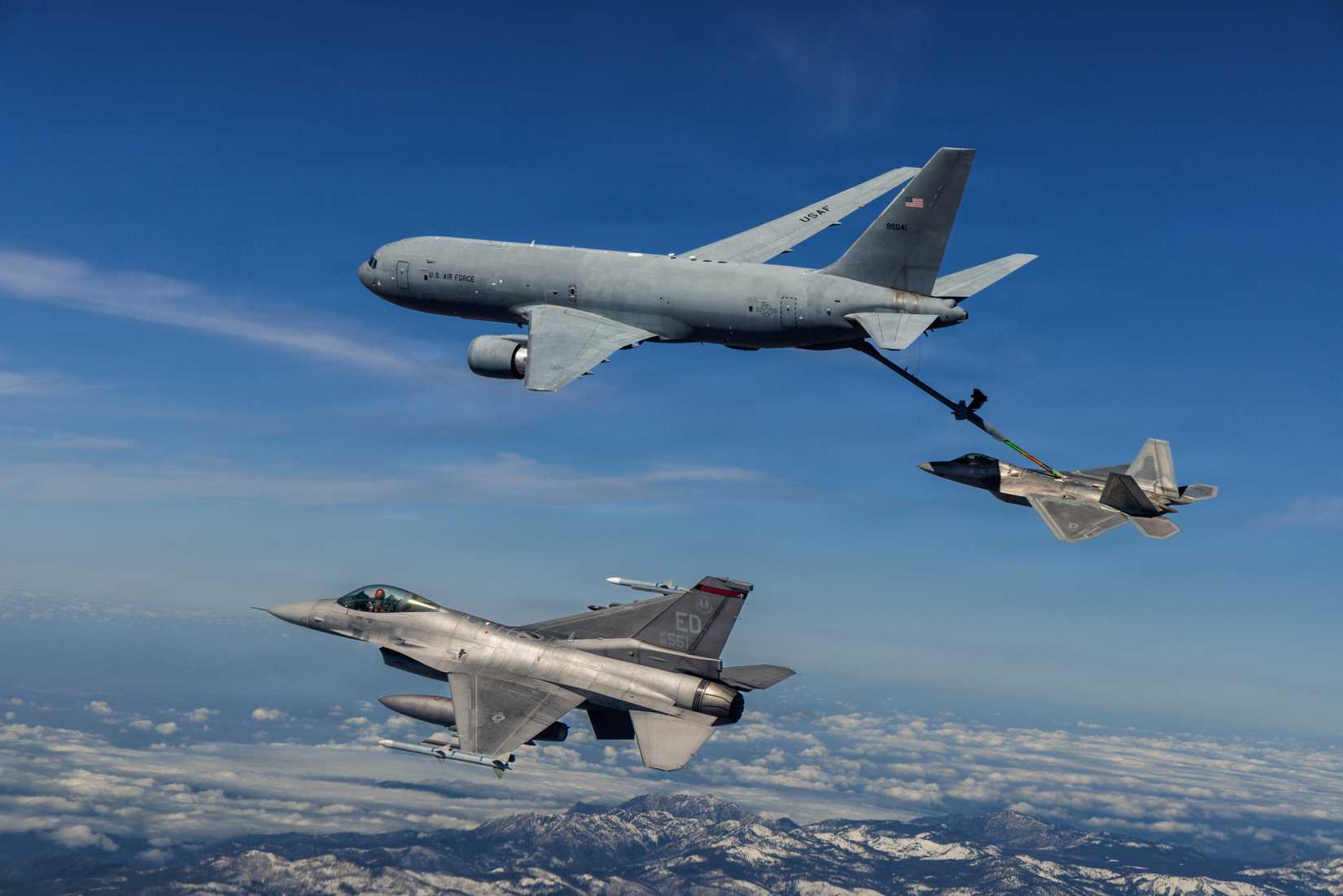 A KC-46 Pegasus refuels an F-22 Raptor while an F-16 waits.