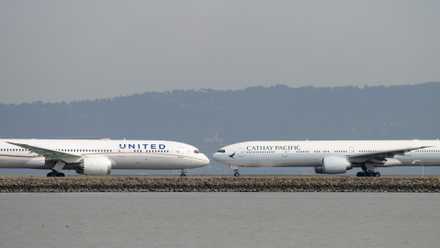 A United Airlines plane taxis towards the end of the runway as a Cathay Pacific airplane taxiis in towards the gate at San Francisco Airport.