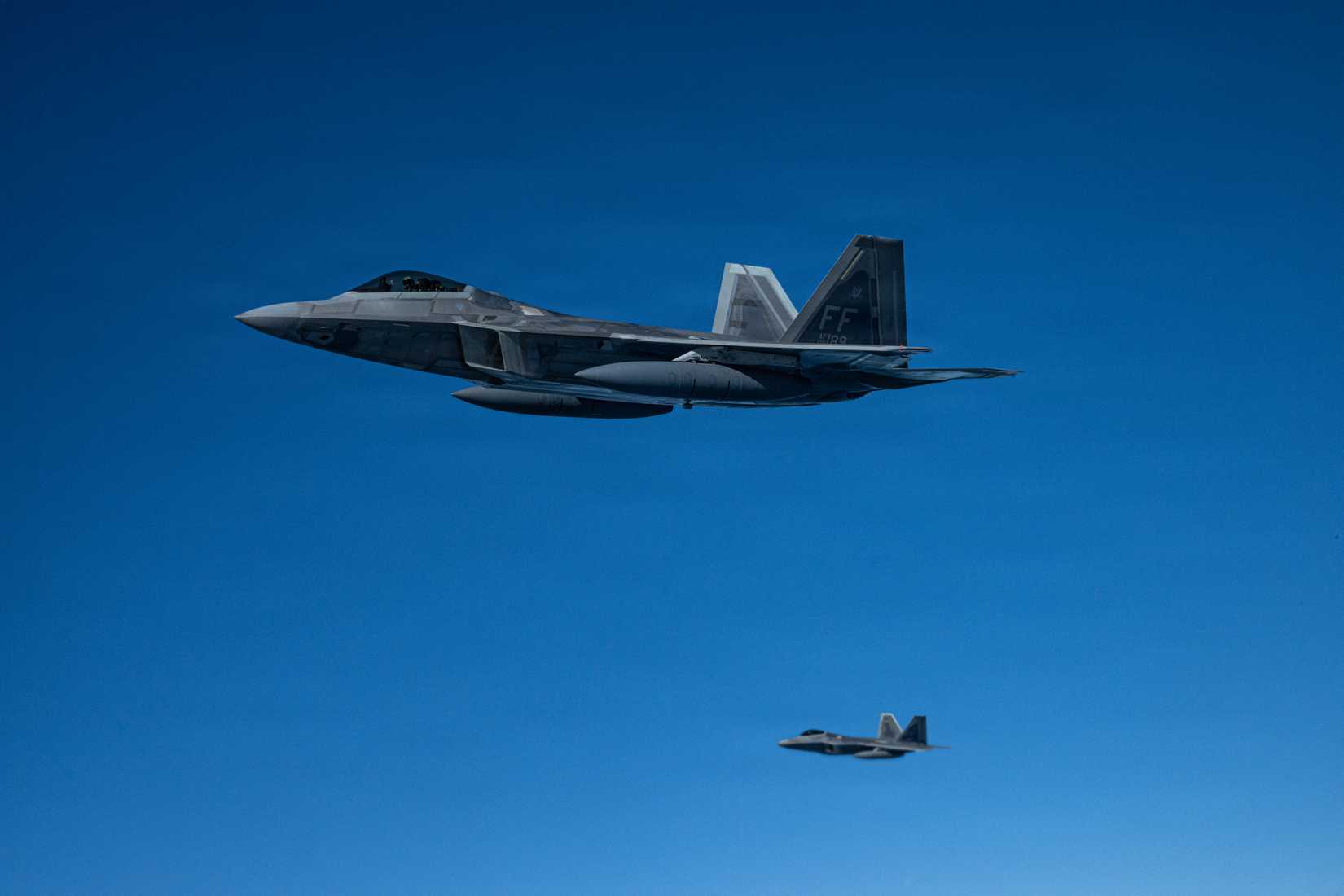 Air Force 1st Fighter Wing F-22 Raptors fly in formation alongside a 100th Air Refueling Wing KC-135 Stratotanker.