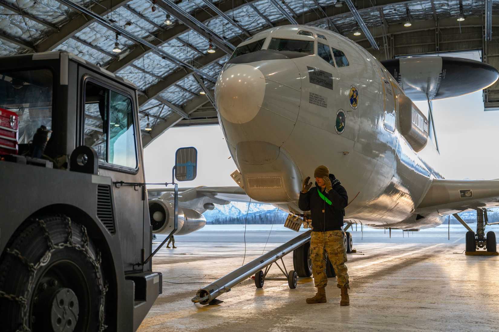 Air Force Tech. Sgt. Jeron Bradshaw, directs a towbar before the aircraft is towed from the hangar at Joint Base Elmendorf-Richardson, Alaska.