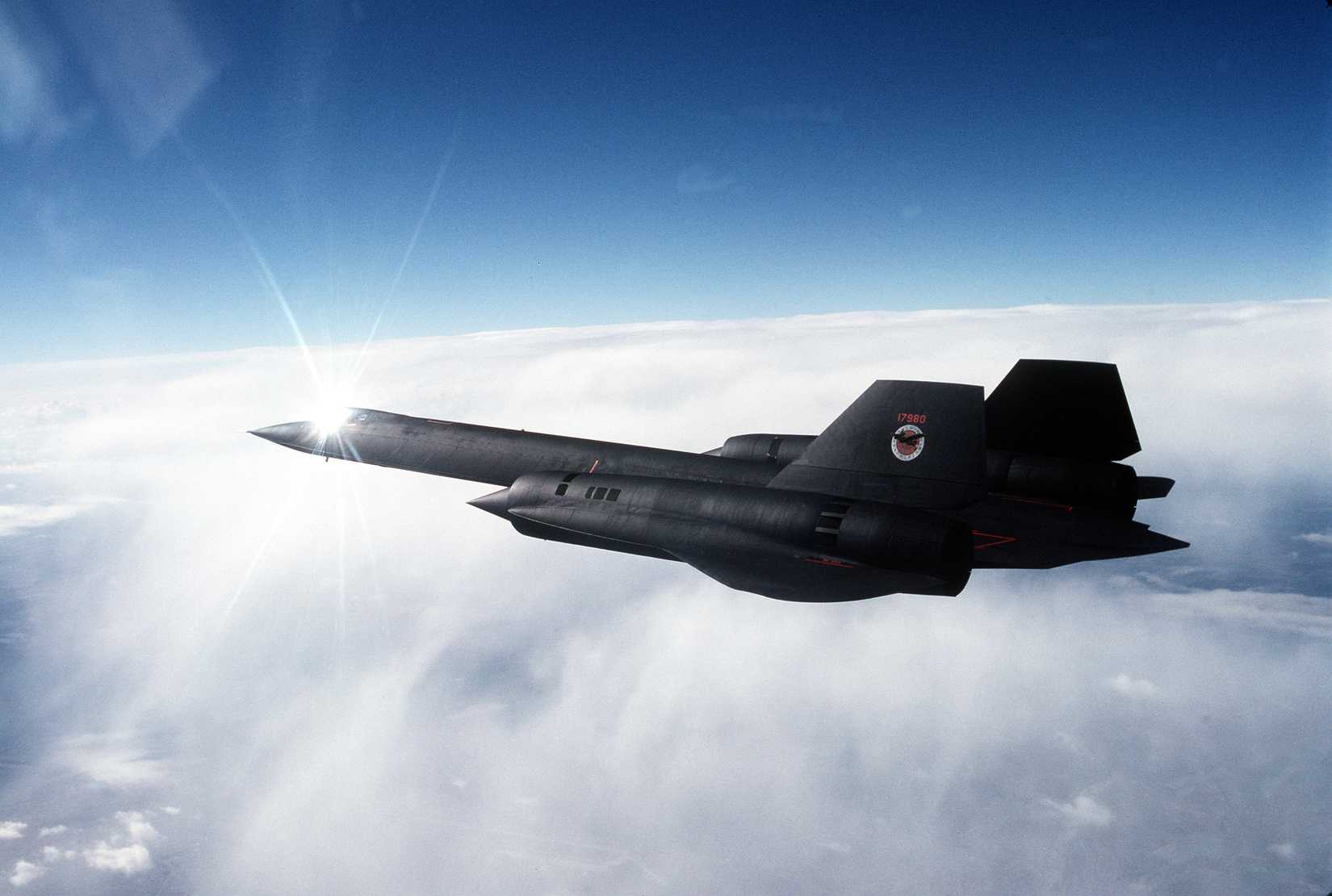 An air-to-air left side view of an SR-71 aircraft over cloud cover.