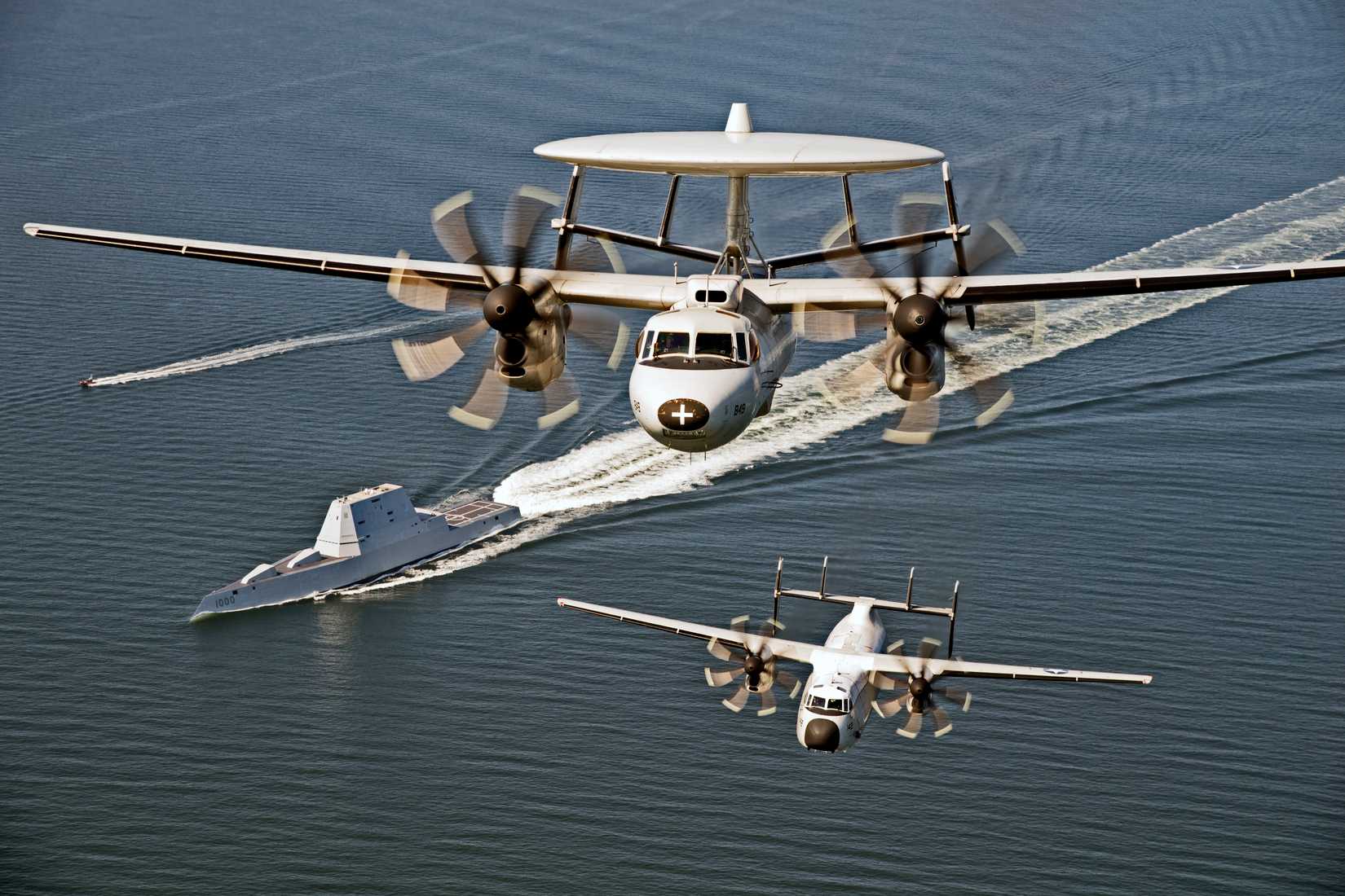 An E-2D Hawkeye and a C-2A Greyhound assigned to VX-20, of NAS Pax River, fly over USS Zumwalt (DDG 1000) as the ship travels to its new home port of San Diego, in 2016.