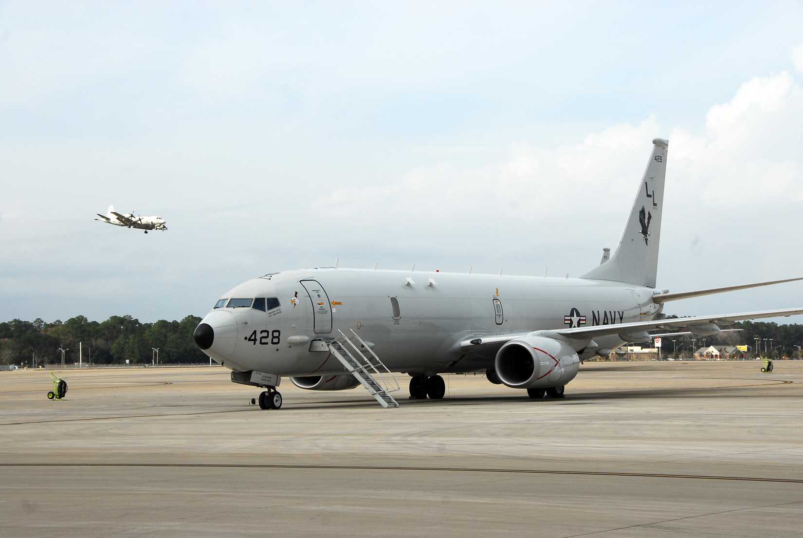 An U.S. Navy P-8A Poseidon aircraft sits on the flight line at Naval Air Station Jacksonville, Fla., as a Navy P-3C Orion aircraft flies in the background Jan. 9, 2013.
