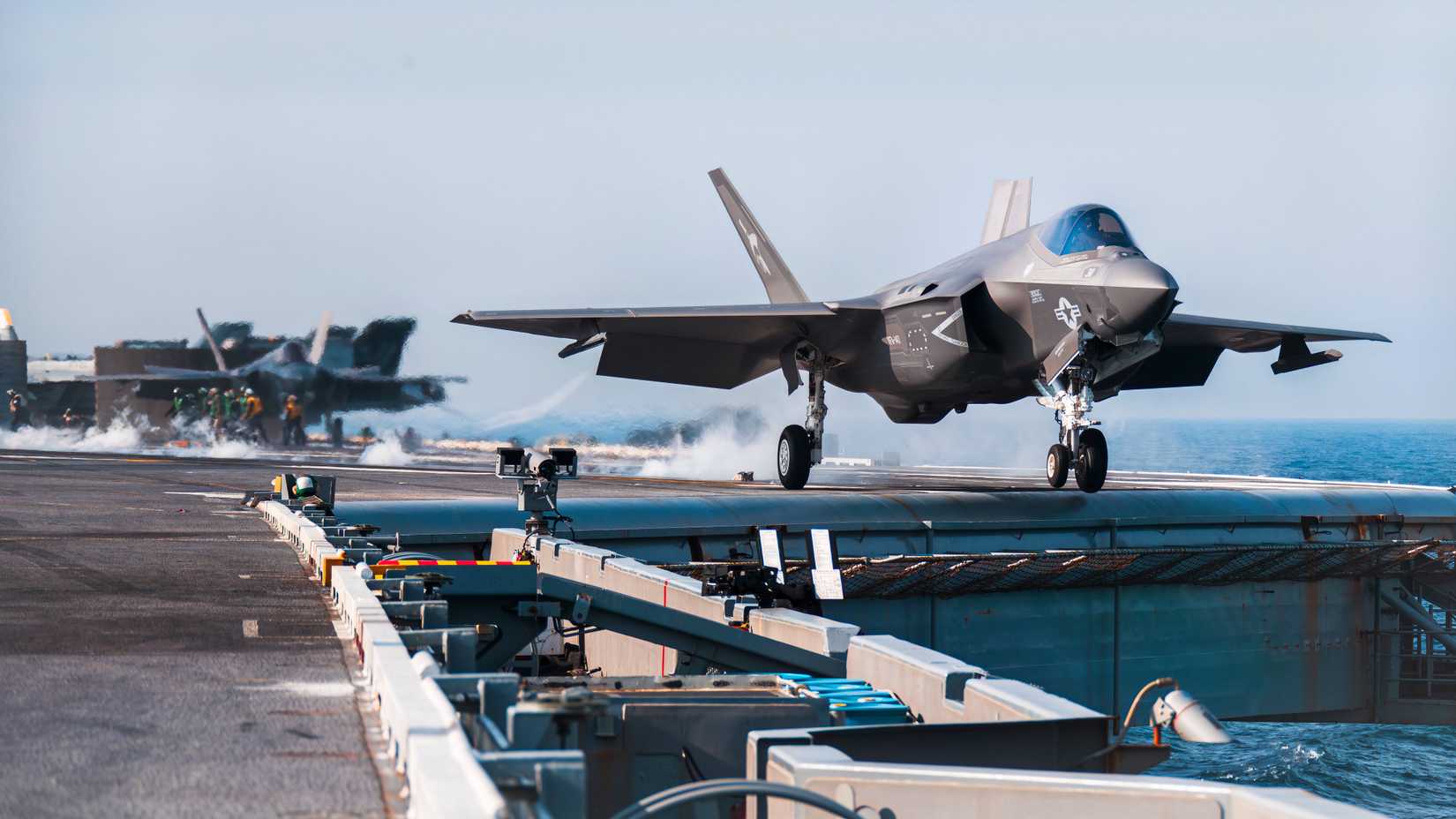 F-35 taking off from the deck of a carrier with more F-35's lined up ready to go.
