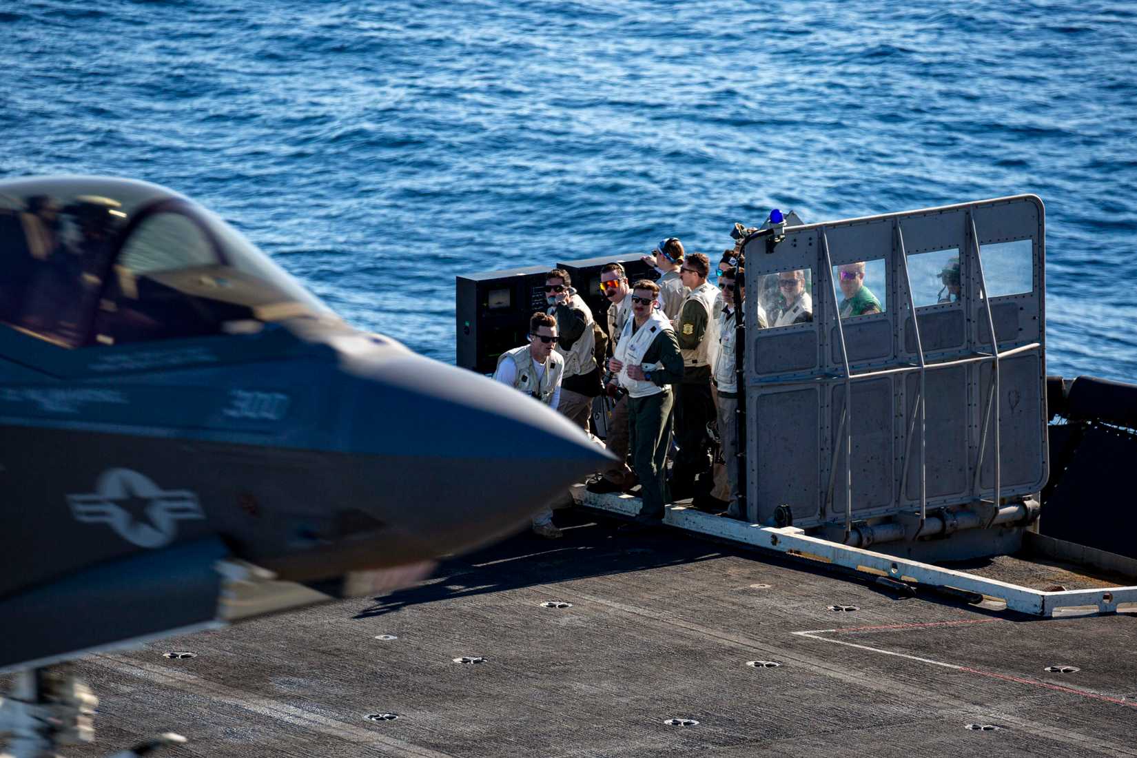 Landing signal officers observe an F-35C Lightning II making an arrested landing on the flight deck.