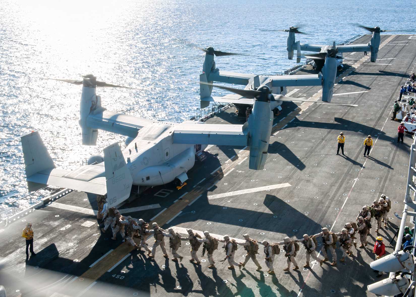 Several MV-22 Osprey's on a flight deck loading up Marines for an operation.