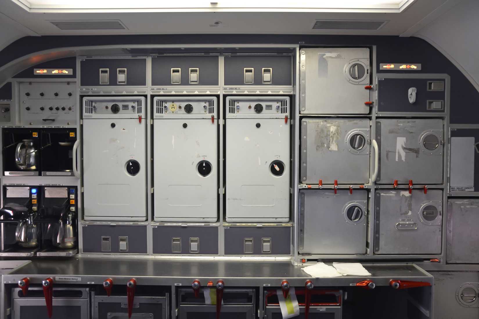 Galley in the back of a commercial aircraft, also know as the kitchen of the airplane. Multiple kitchen accessories in metal like steel and aluminium. Coffee makers visible