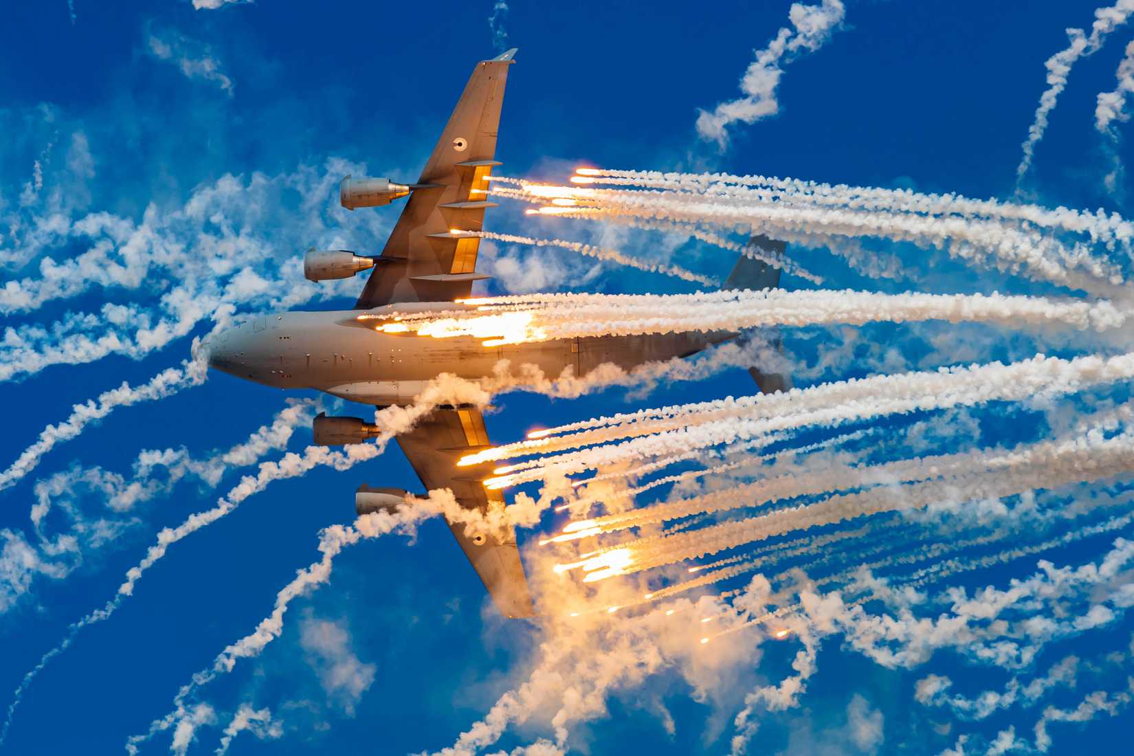 A military cargo aircraft (C-17) dispenses flares at the airshow to show its defense capabilities 