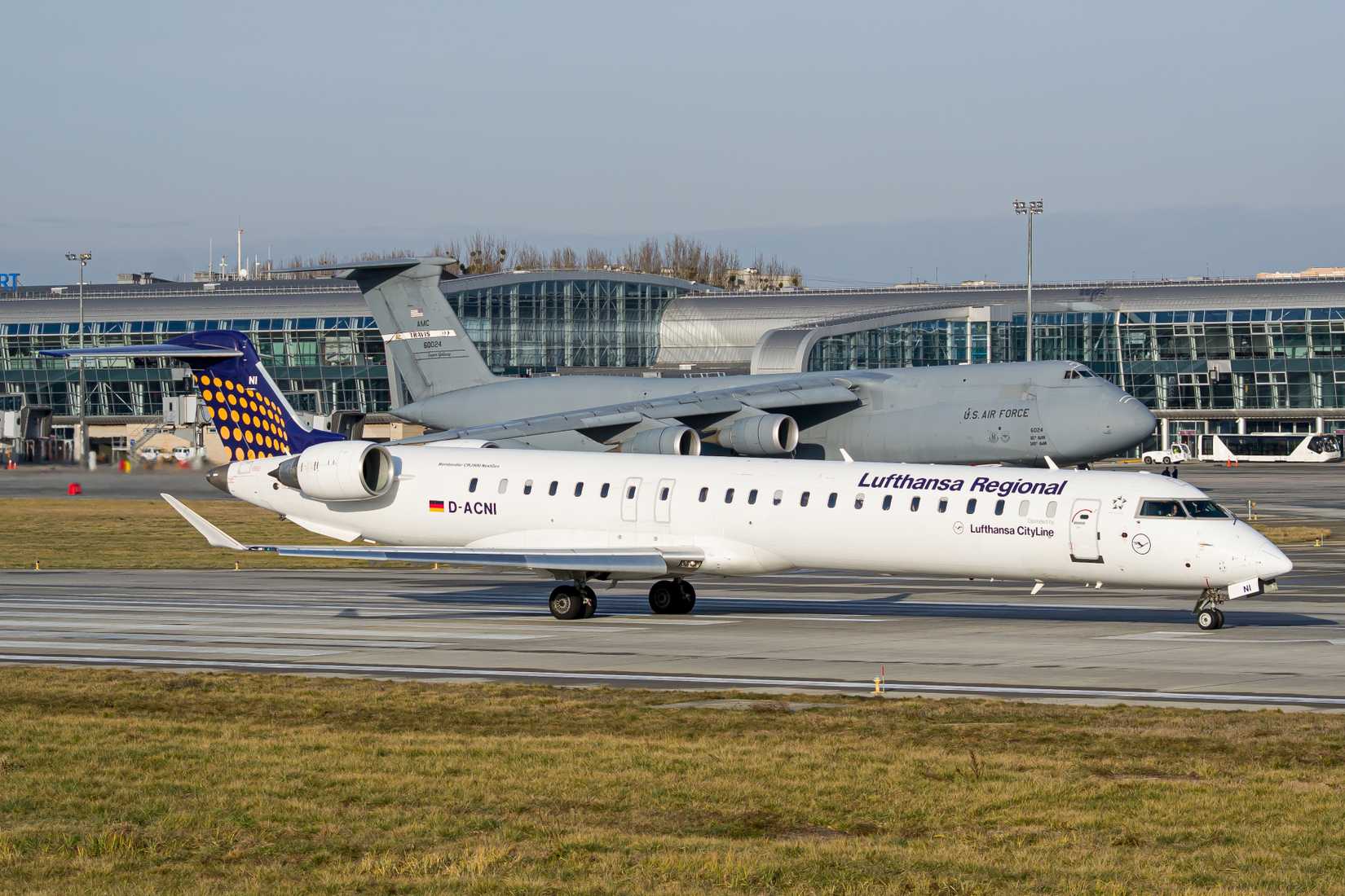Lviv, Ukraine - December 16th, 2019: Lufthansa Regional Bombardier CRJ-900 NextGen taxiing for takeoff from Lviv with US Air Force C-5 Galaxy in the background