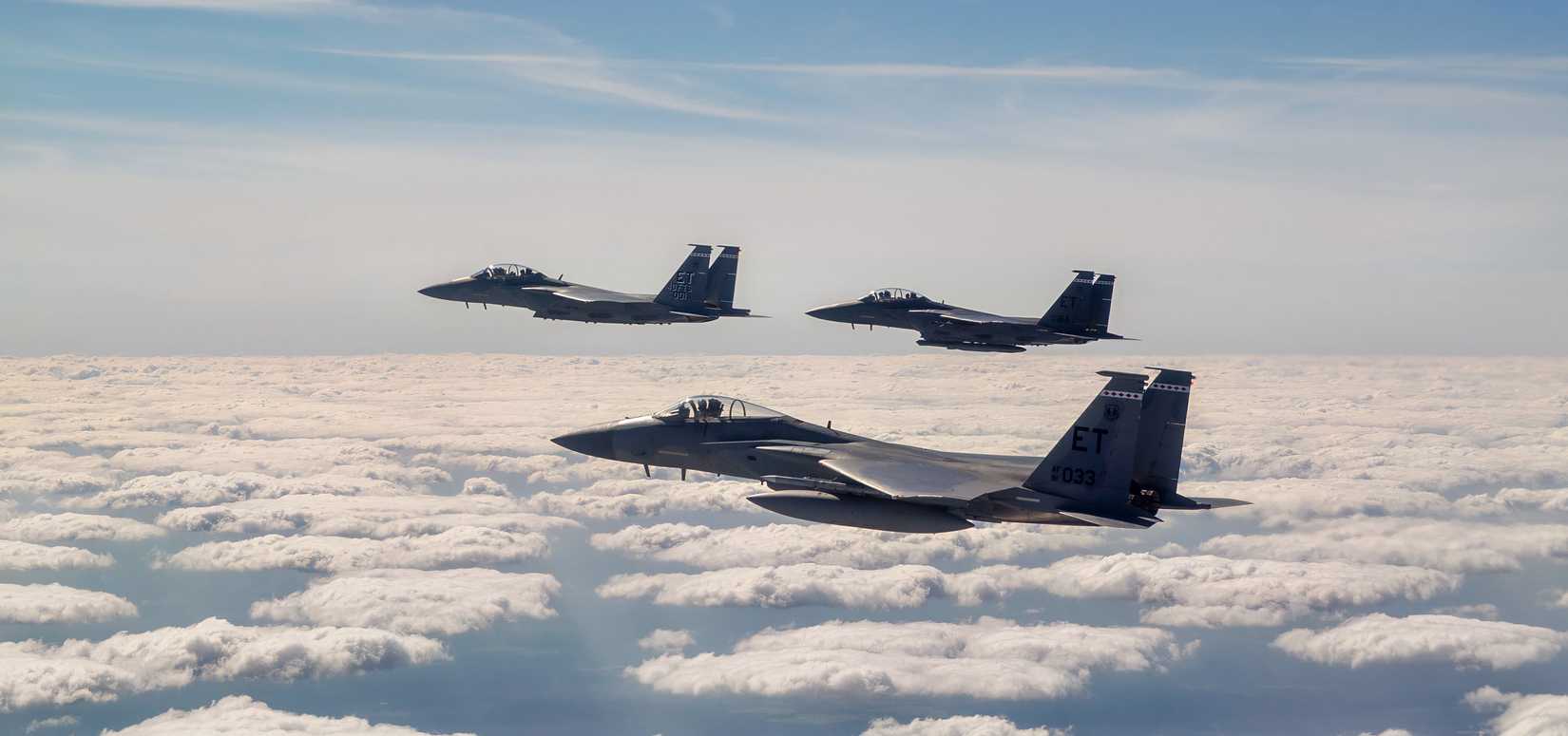 Three F-15s flying in formation above the coulds.