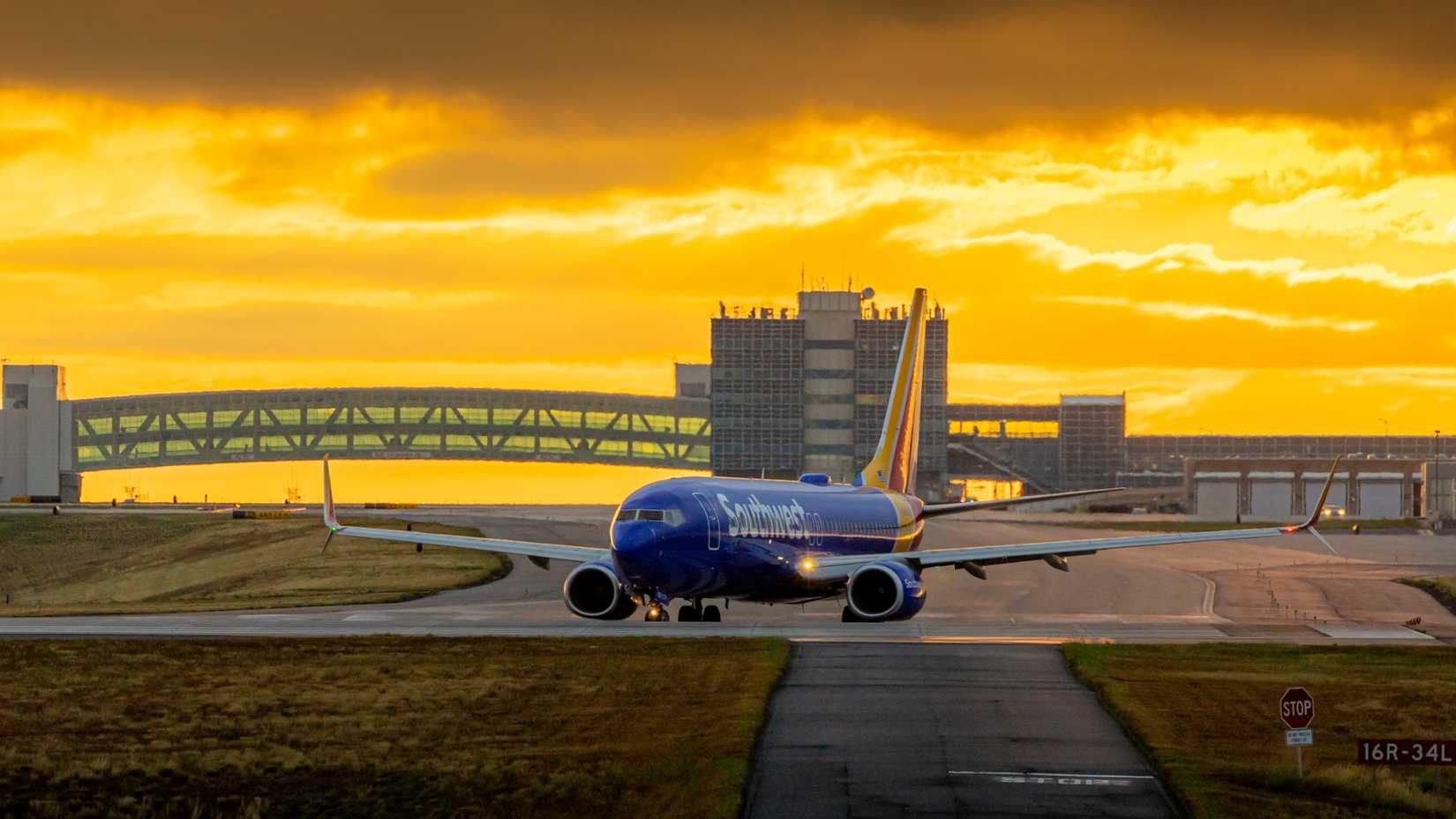 A blue Southwest Airlines airplane taxis on an airport runway with a golden sunset in the background.