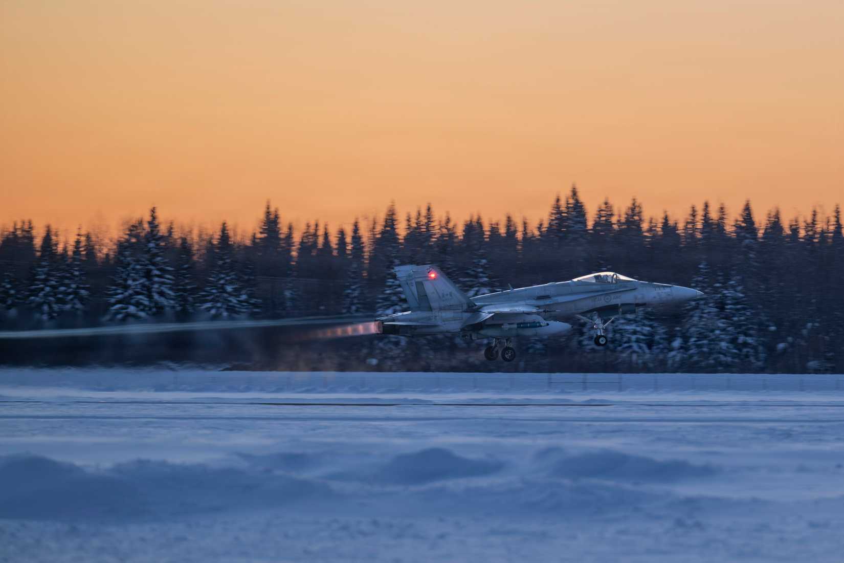 A CF-188 Hornet assigned to Canadian Air Task Force departs the runway in Arctic winter conditions with snow-covered mountains in the background during Exercise Arctic Edge 26.