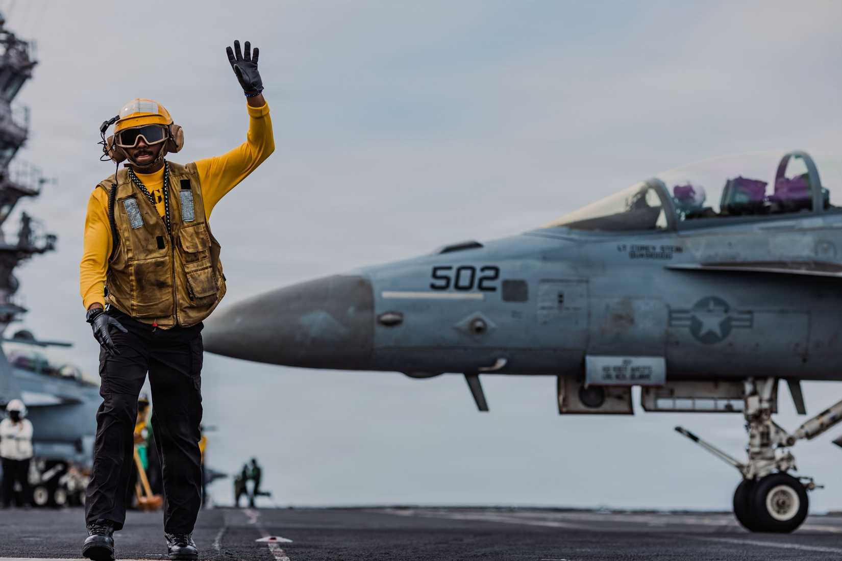 ailor signals to the pilot of an EA-18G Growler aircraft, attached to Electronic Attack Squadron 142, during flight operations on the flight deck.