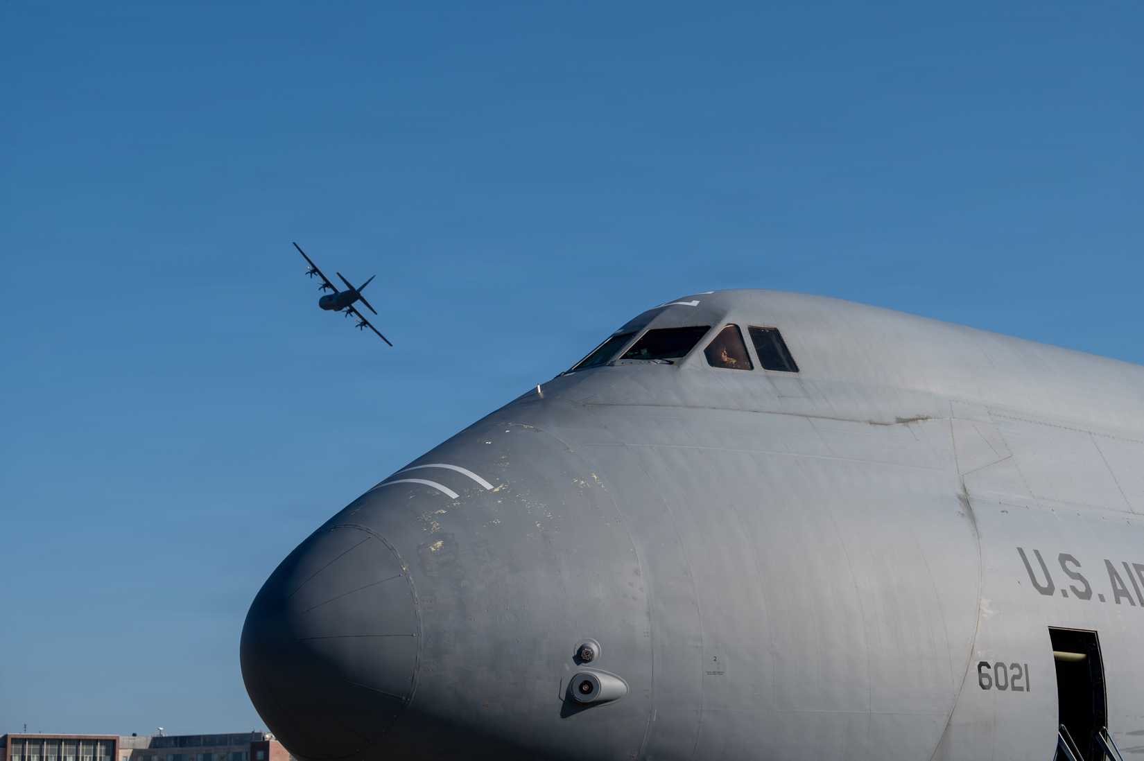 Air Force C-5M Super Galaxy sits on the flight line while a C-130 Super Hercules flies overhead at Ramstein Air Base, Germany, March 4, 2026.
