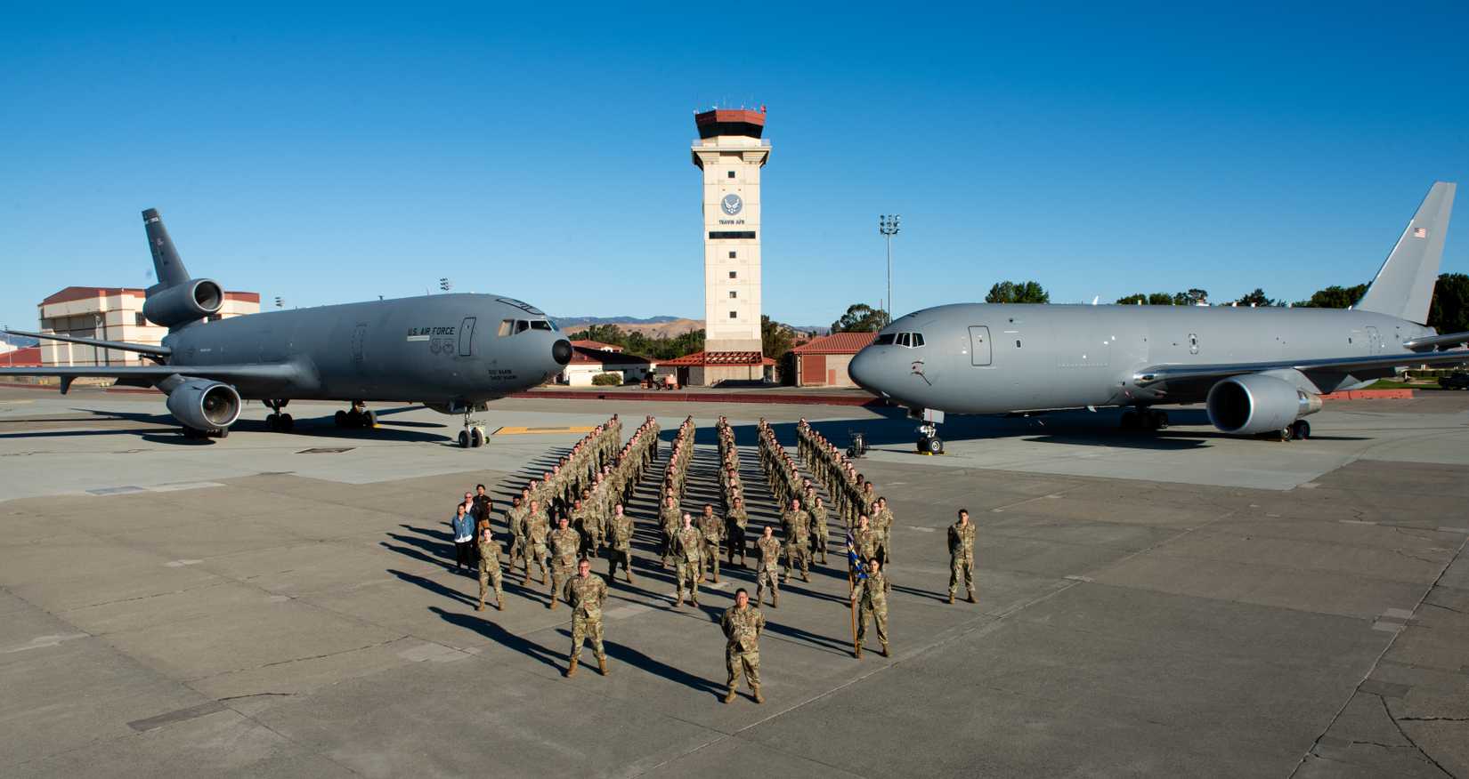 Airmen assigned to the 660th Aircraft Maintenance Squadron stand in formation in front of a KC-10 Extender and KC-46A Pegasus on the flight line at Travis Air Force Base.