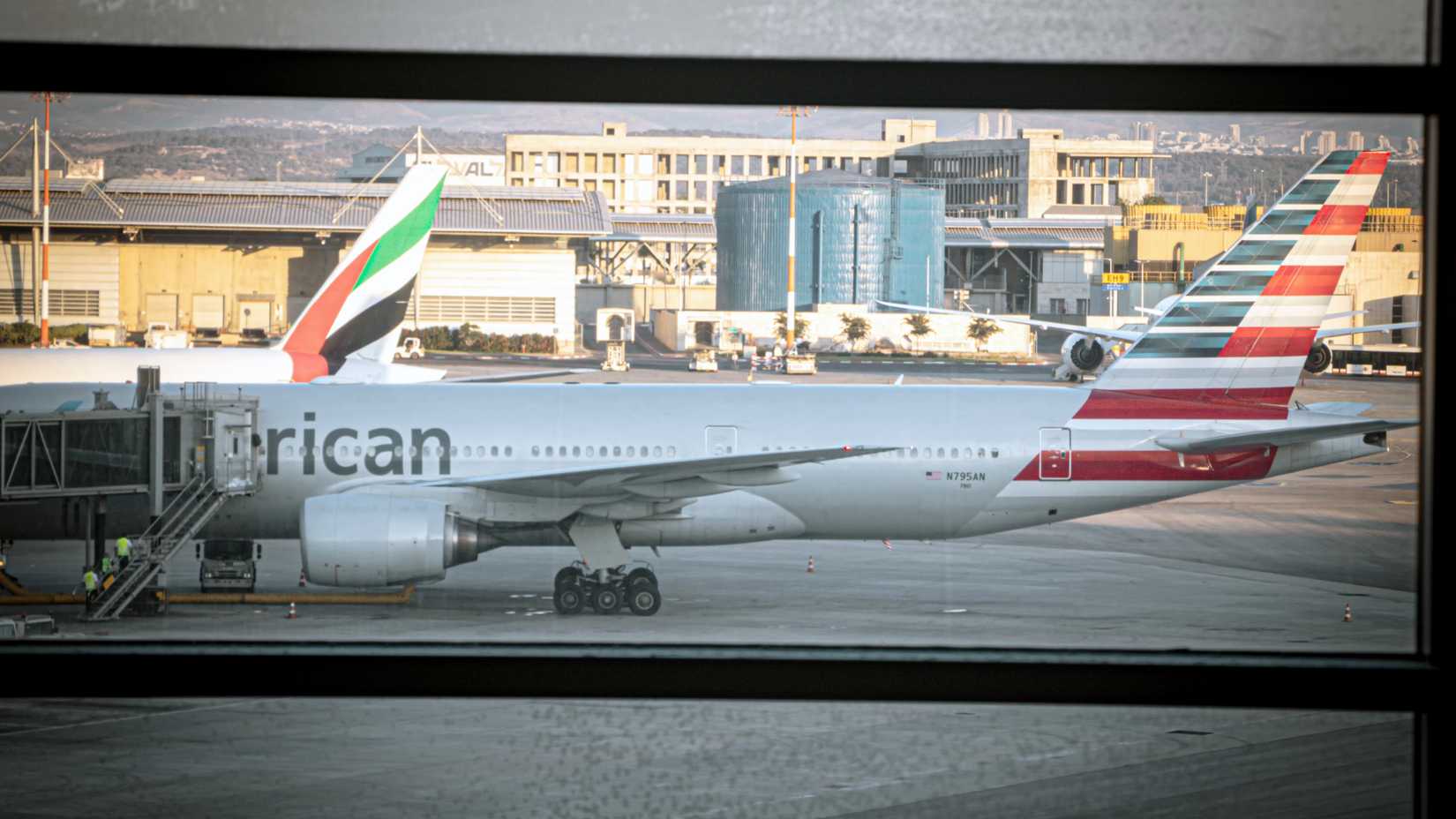 An American Airlines Boeing 777-200 is parked at the gate next to an Emirates Boeing 777-300 at Ben Gurion Airport