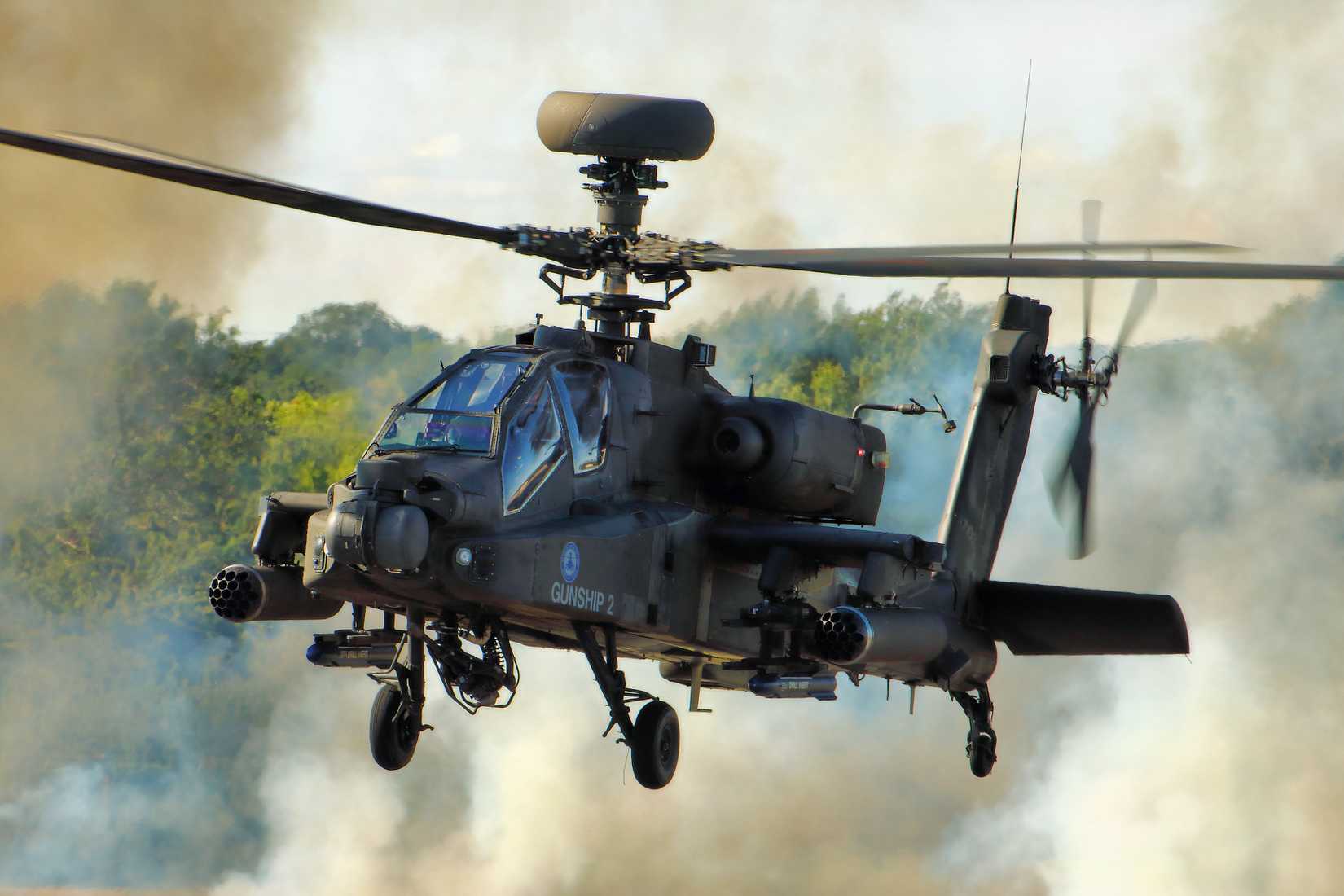 An Apache helicopter hovering with smoke in the background.