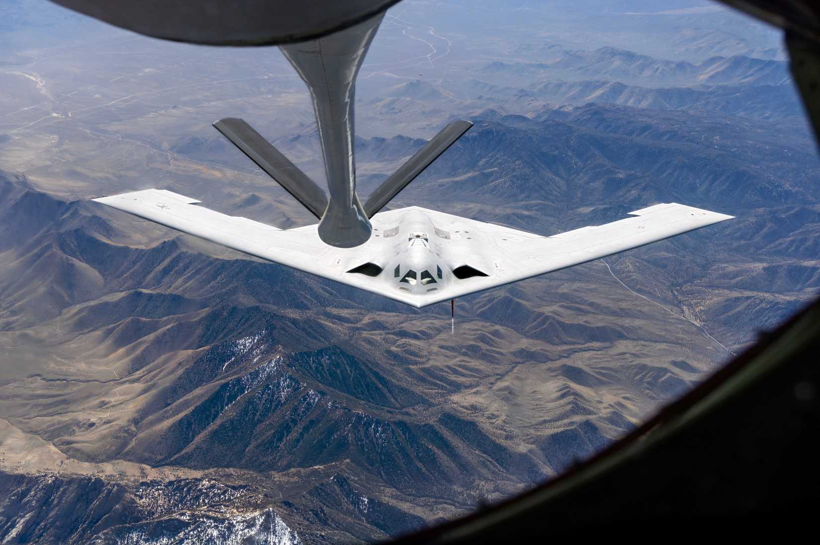 Image of a B-21 preparing to refuel, flying over a mountain range.