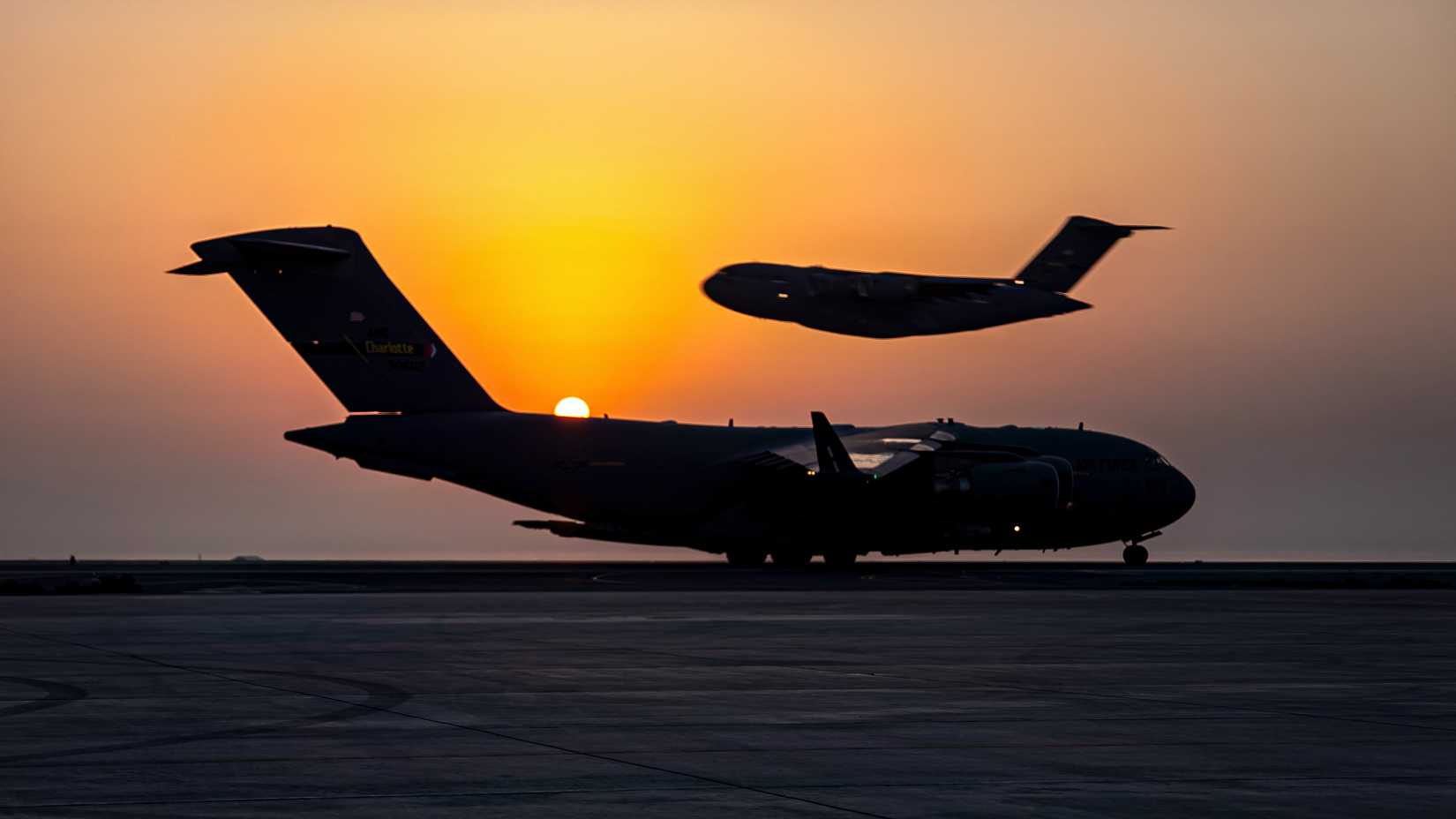 C-17's at an airbase in the evening. One is on the runway, another is taking-off in the background. 