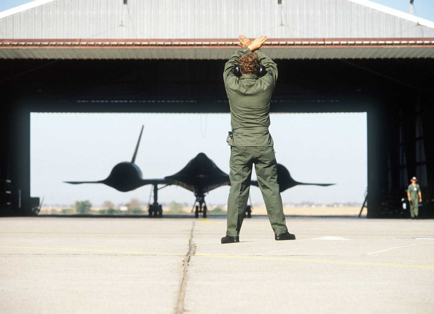 Crew SSGT David L. Hansen directs an SR-71 Blackbird aircraft out of a hangar. The aircraft, from the 9th Strategic Reconnaissance Wing, will be refueled by a KC-10 Extender aircraft in flight during testing.
