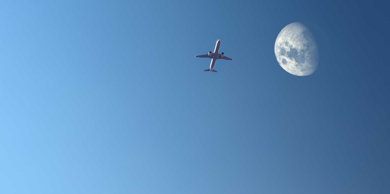 Airplane rising towards the moon in the cloudless dark blue sky in the evening.