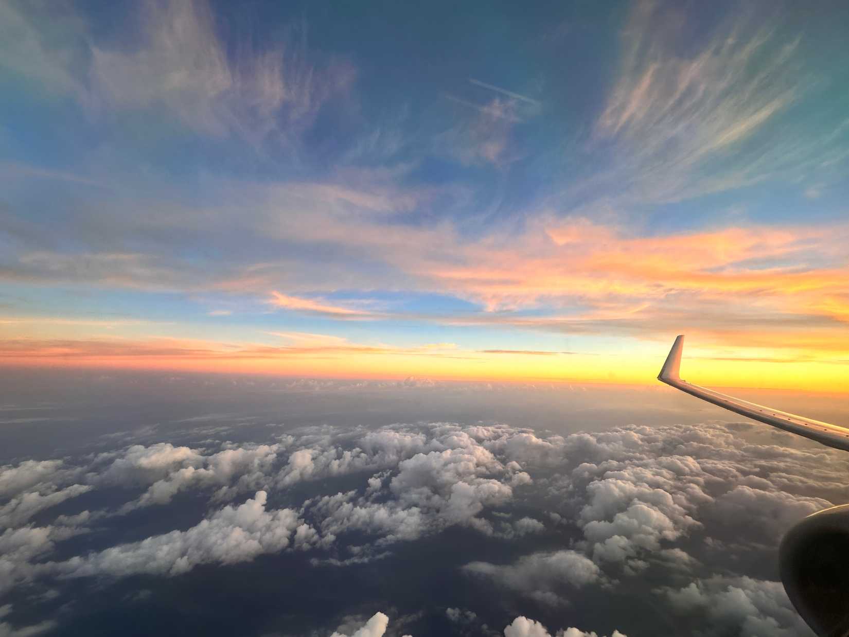 A picture of the sunset taken from a plne hovering over clouds somewhere in the ocean